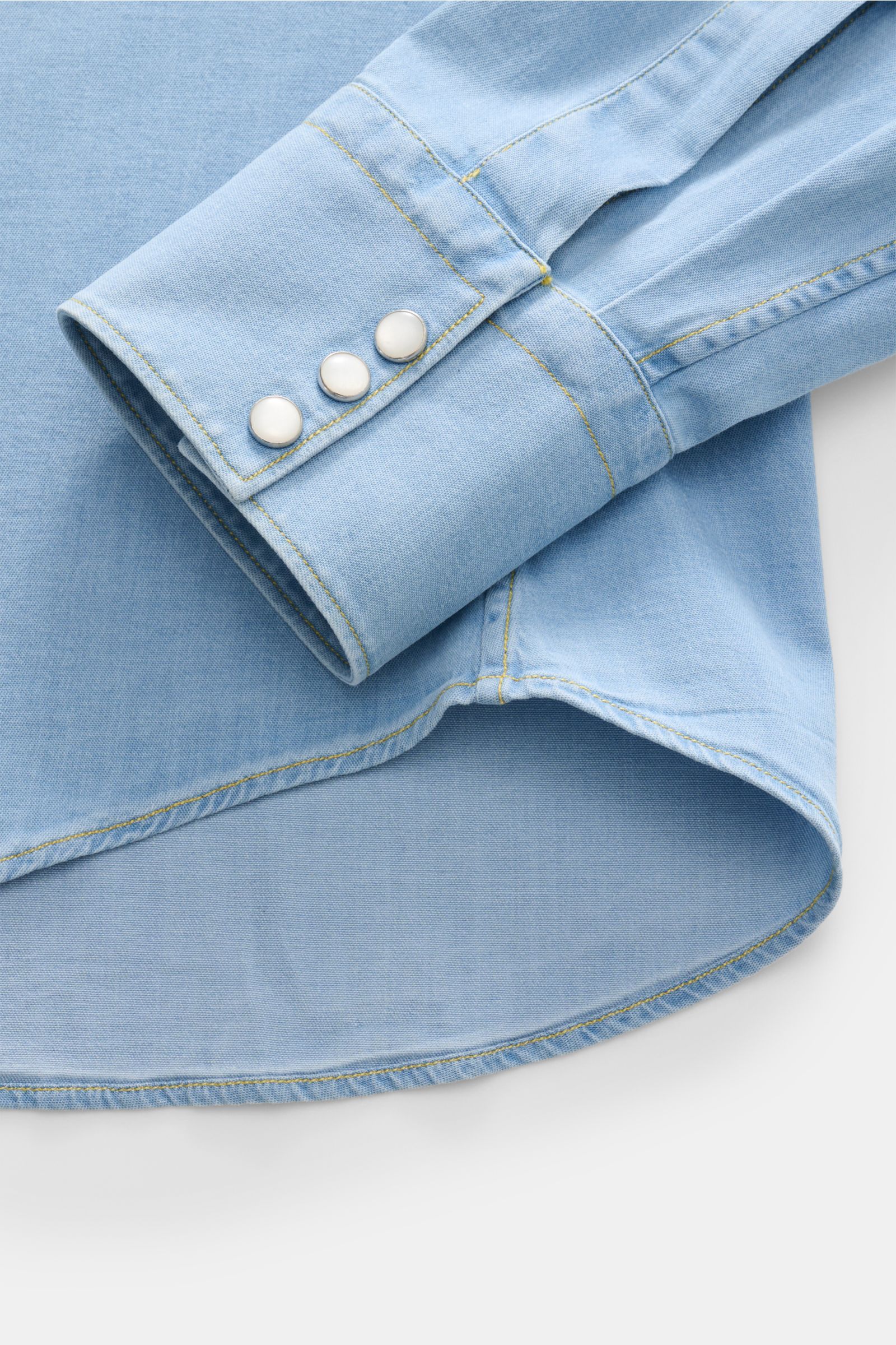 Close-up from above of the sleeve and hem of the Gherardi Chambray-Hemd Kent-Kragen hellblau, a slim fit, soft, elastic cotton chambray shirt in denim look with Western-style yoke, snap button placket, chest pockets, sport cuffs with snap buttons, and rou