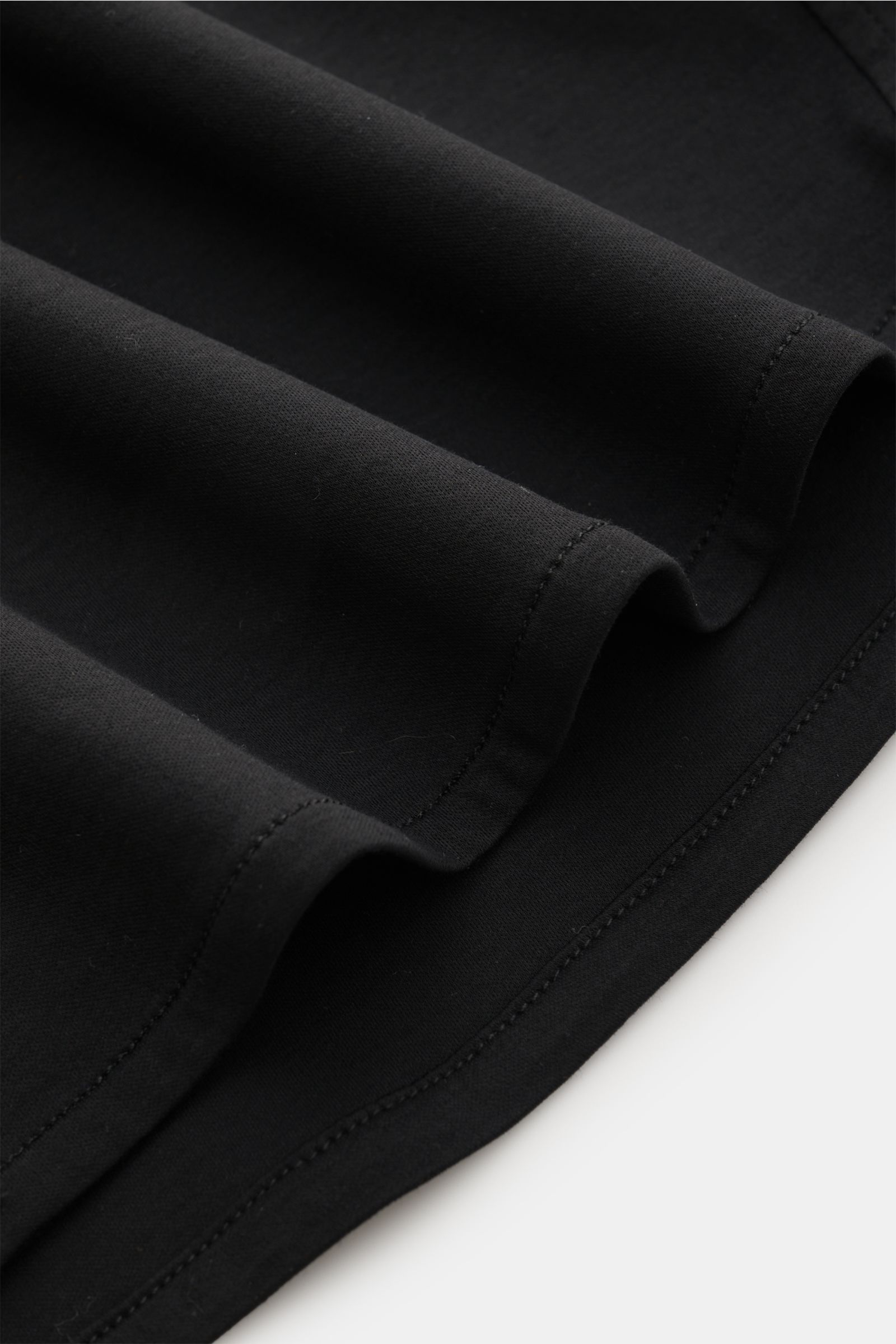 Nahaufnahme des Kiefermann Jersey-Hemd 'Pius' Kent-Kragen schwarz Saums aus mercerisierter Baumwolle mit weichem Griff, dezentem Glanz, Extra Slim Fit, französischer Knopfleiste und leicht gerundetem Saumverlauf, fotografiert von unten.