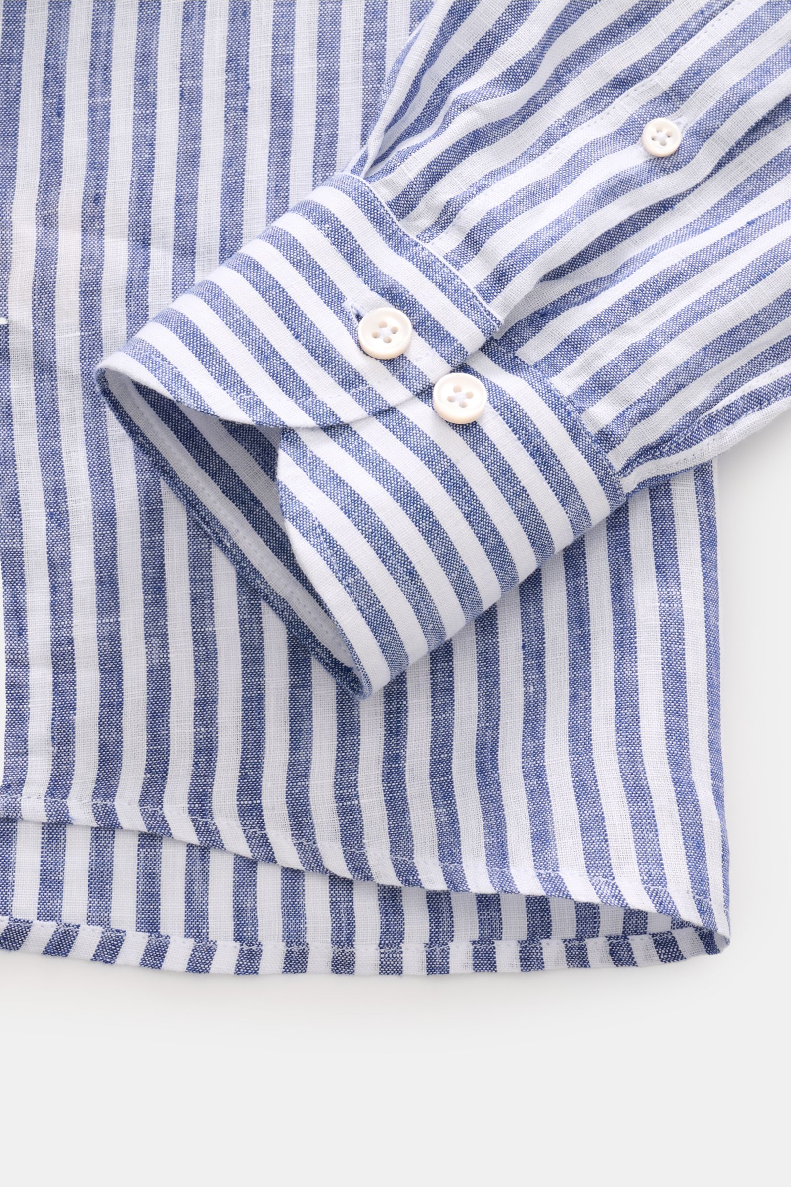 Close-up front view of the cuff and hem of the Aurélien Leinenhemd Haifisch-Kragen navy/weiß gestreift, a slim fit linen shirt with soft texture, shark collar, French button placket, classic sport cuffs, back waist darts, and rounded hem, perfect for offi