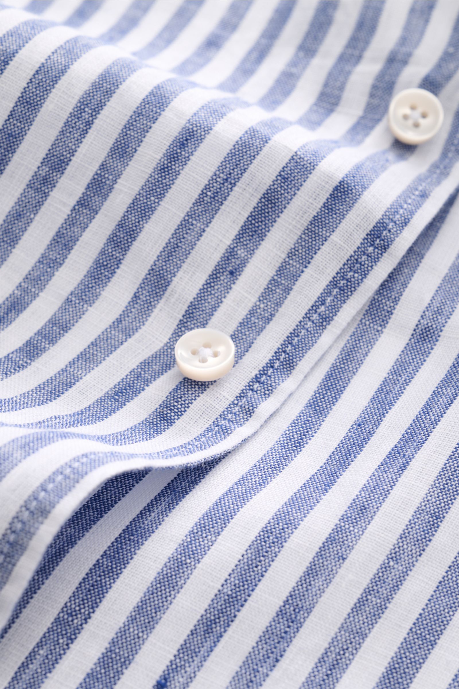 Close-up image of the Aurélien Leinenhemd Haifisch-Kragen navy/weiß gestreift, showing fine linen fabric with navy and white stripes and white buttons from a top front perspective. Ein wenig Urlaubsfeeling gefällig? Das vielseitig einsetzbare Hemd der 