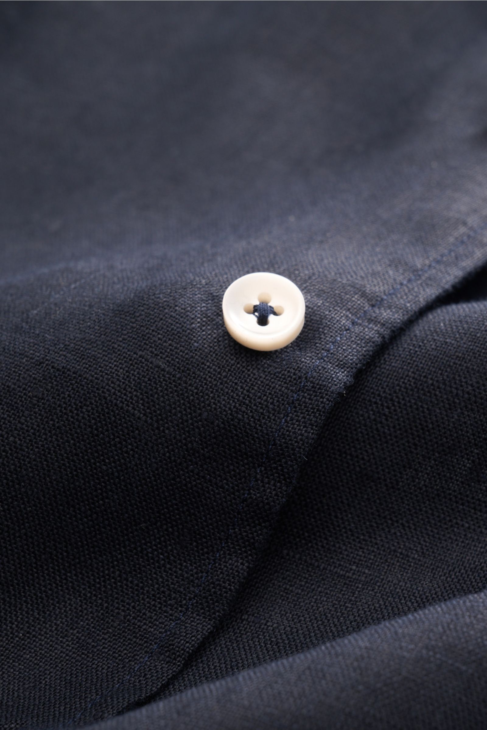 Alt tag (125 characters): Close-up from above of a white button on the dark navy Aurélien Linen shirt shark collar dark navy showing fabric texture.

Want to get into the holiday mood? With its fine linen fabric, this versatile shirt by the brand AURÉL