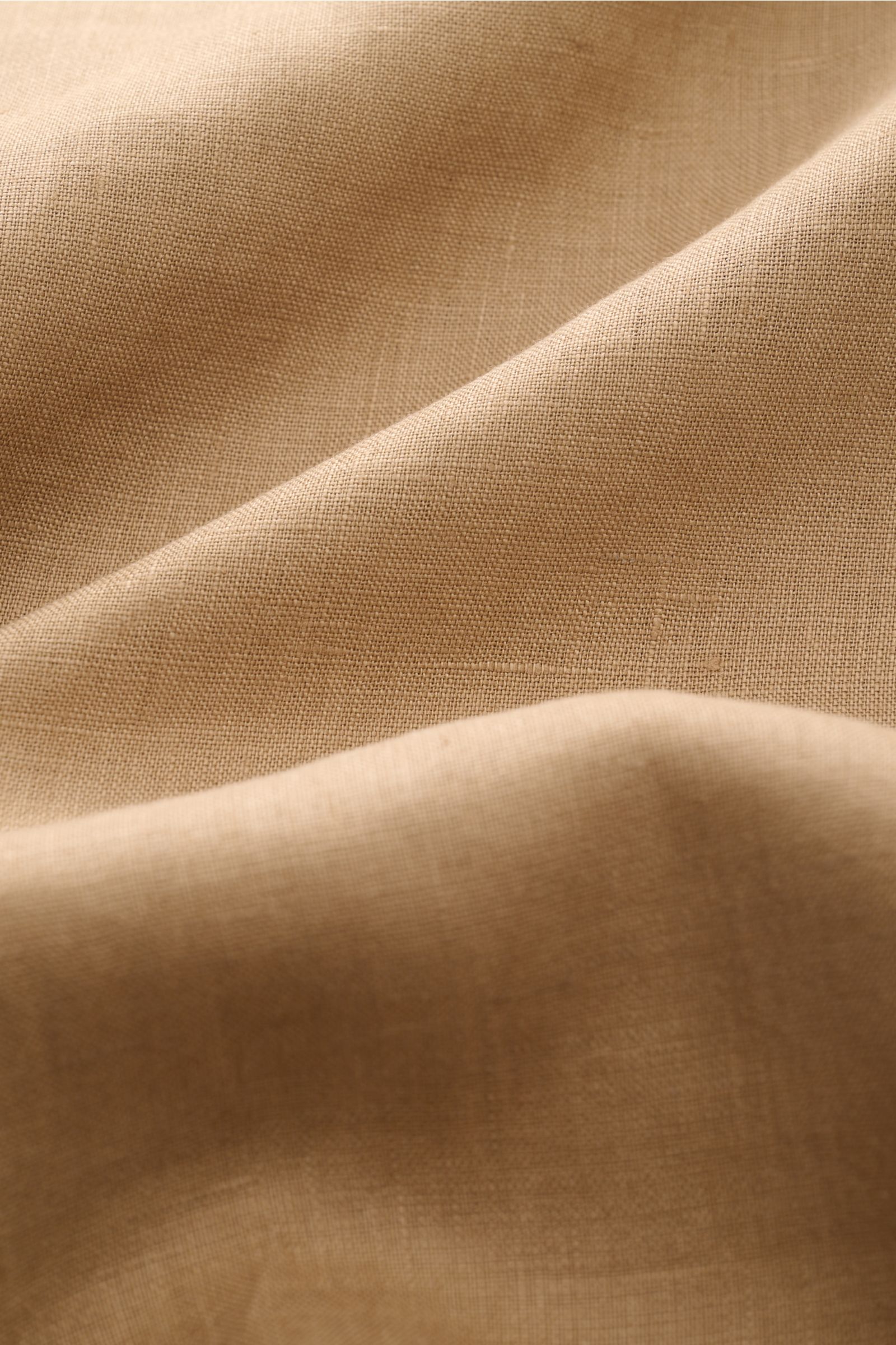 Close-up front view of the sand-colored Aurélien Leinenhemd Haifisch-Kragen showing fine linen fabric texture and soft folds. 

Ein wenig Urlaubsfeeling gefällig? Das vielseitig einsetzbare Hemd der Marke AURÉLIEN wird mit seinem feinen Leinengewebe zu