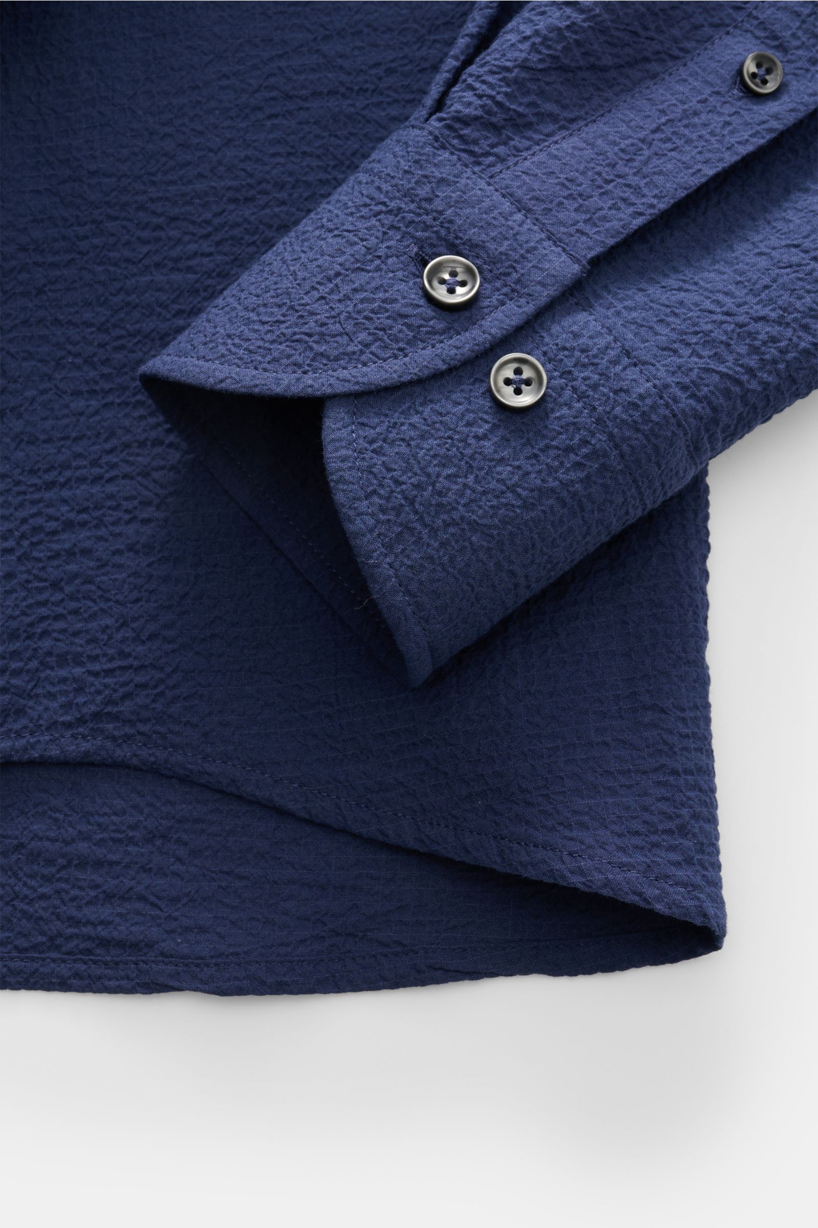 Close-up front view of the Aurélien Seersucker-Hemd Haifisch-Kragen dunkelblau showing the textured dark blue cotton fabric, slim fit cuff with two buttons, and slightly rounded hem.

Sommerlicher Eyecatcher: Das Hemd von AURÉLIEN überzeugt mit charakt