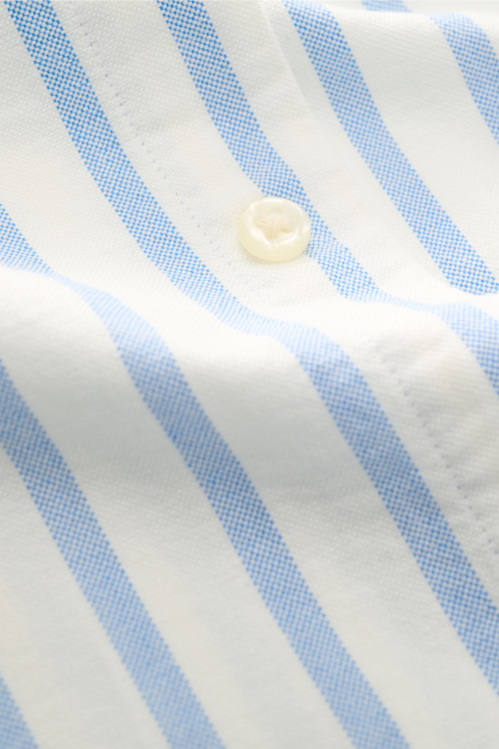 Close-up of a white button on the blue and white striped fabric of the Polo Ralph Lauren Casual Hemd Button-Down-Kragen blau/weiß gestreift, photographed from a top angle showing the fabric texture and stitching details.

Stilvoll durch den Sommer: Das