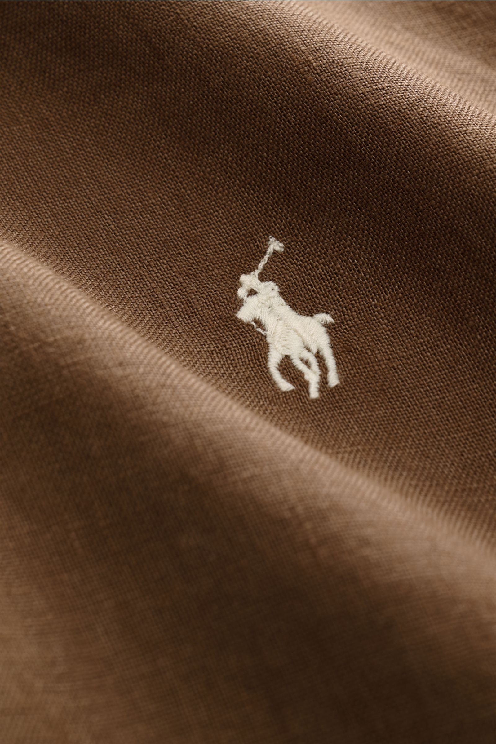 Close-up of Polo Ralph Lauren Leinenhemd Button-Down-Kragen braun fabric with detailed white polo player embroidery, showing linen texture from a top-side perspective. Dieses Leinenhemd von POLO RALPH LAUREN ist eine Bereicherung für jede Sommergardero