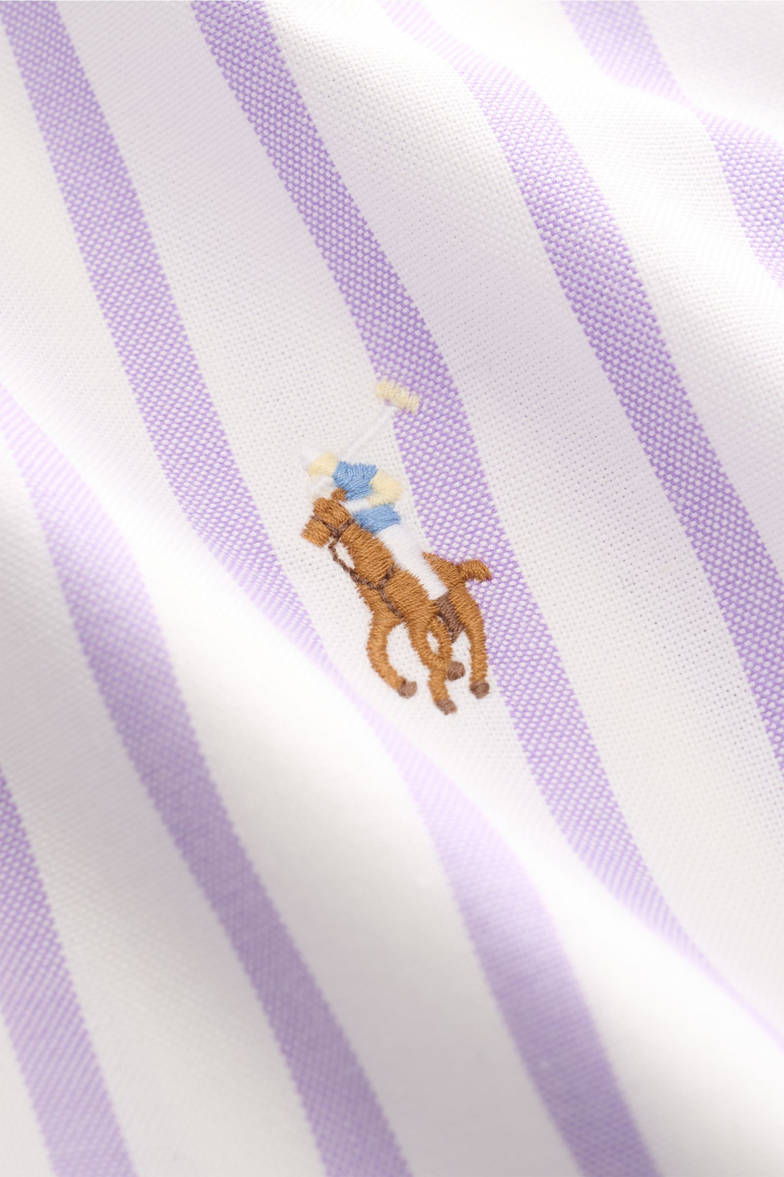 Close-up front view of Polo Ralph Lauren Casual Hemd Button-Down-Kragen flieder/weiß gestreift fabric showing lilac and white stripes with embroidered polo player logo.

Stilvoll durch den Sommer: Das Slim-Fit-Hemd von POLO RALPH LAUREN ergänzt Ihre Ga