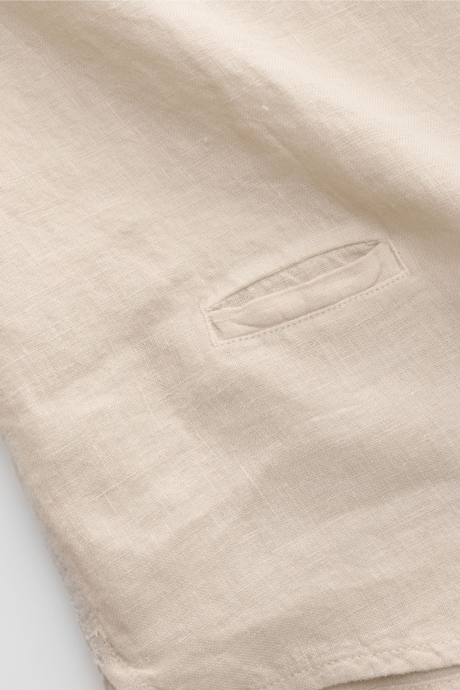 Close-up view of the sand-colored 04651/ A trip in a bag Leinenhemd schmaler Kragen sand linen shirt fabric showing fine texture and a small pocket detail. Mühelose Leichtigkeit