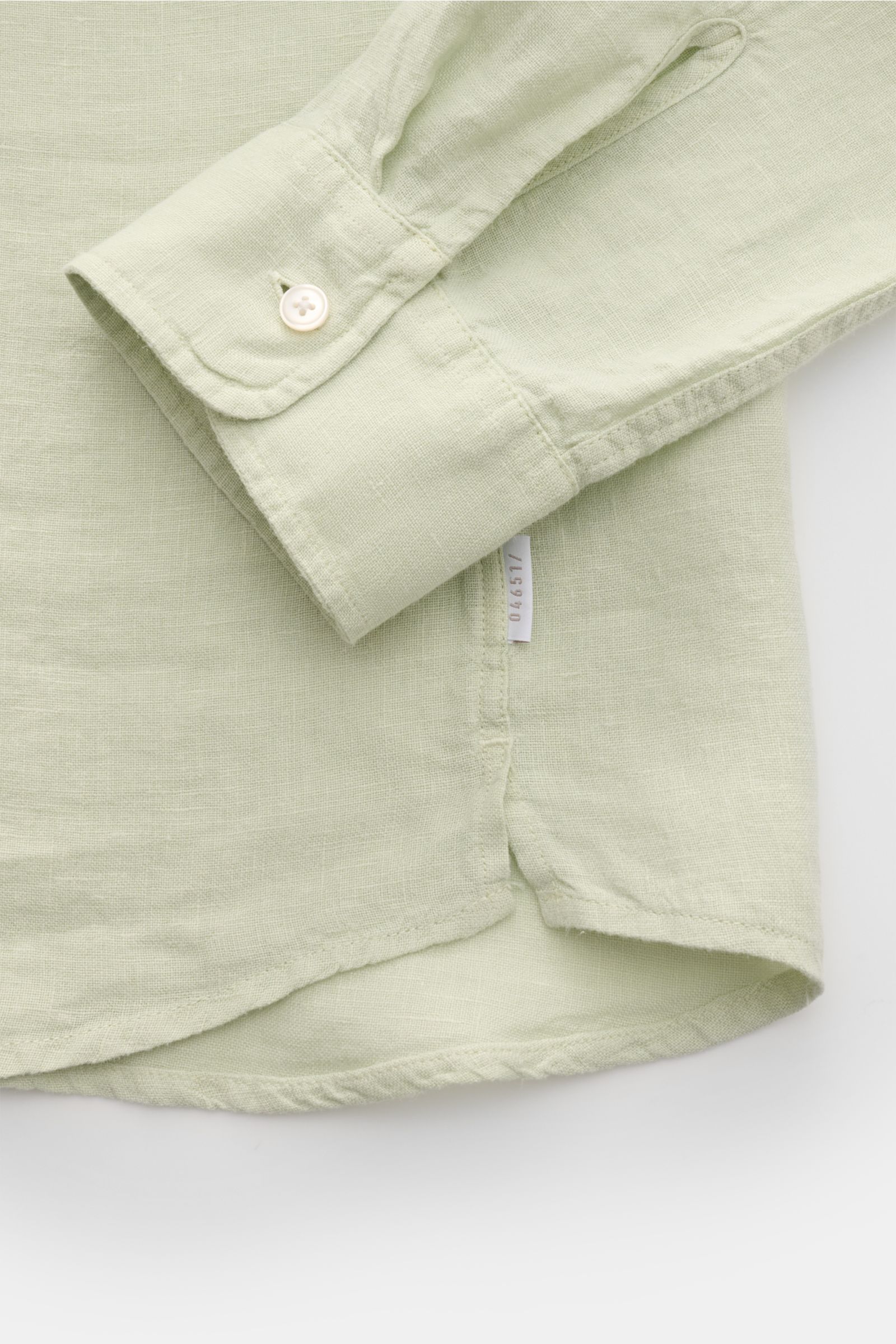 Close-up view of the cuff and hem of the 04651/ A trip in a bag Leinenhemd schmaler Kragen pastellgrün, showing light green pure linen fabric with material-typical texture, a single button on the classic sports cuff, small side seam label, slightly rounde