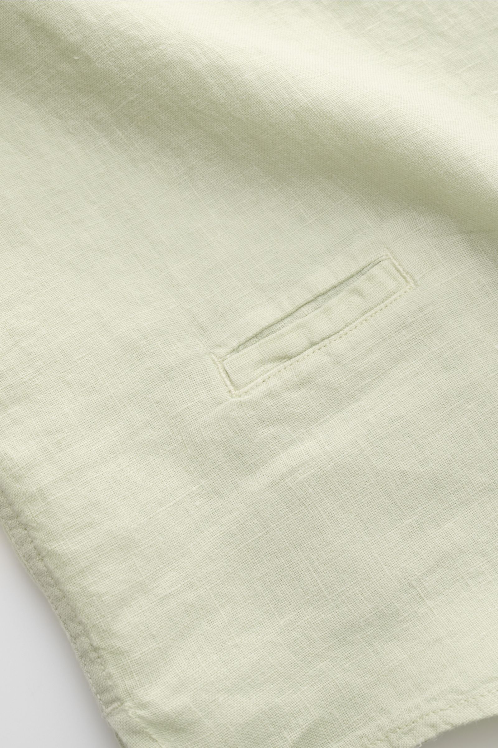 Close-up front view of the pastel green “04651/ A trip in a bag Leinenhemd schmaler Kragen pastellgrün” showing pure linen fabric texture and a small welt pocket. Mühelose Leichtigkeit