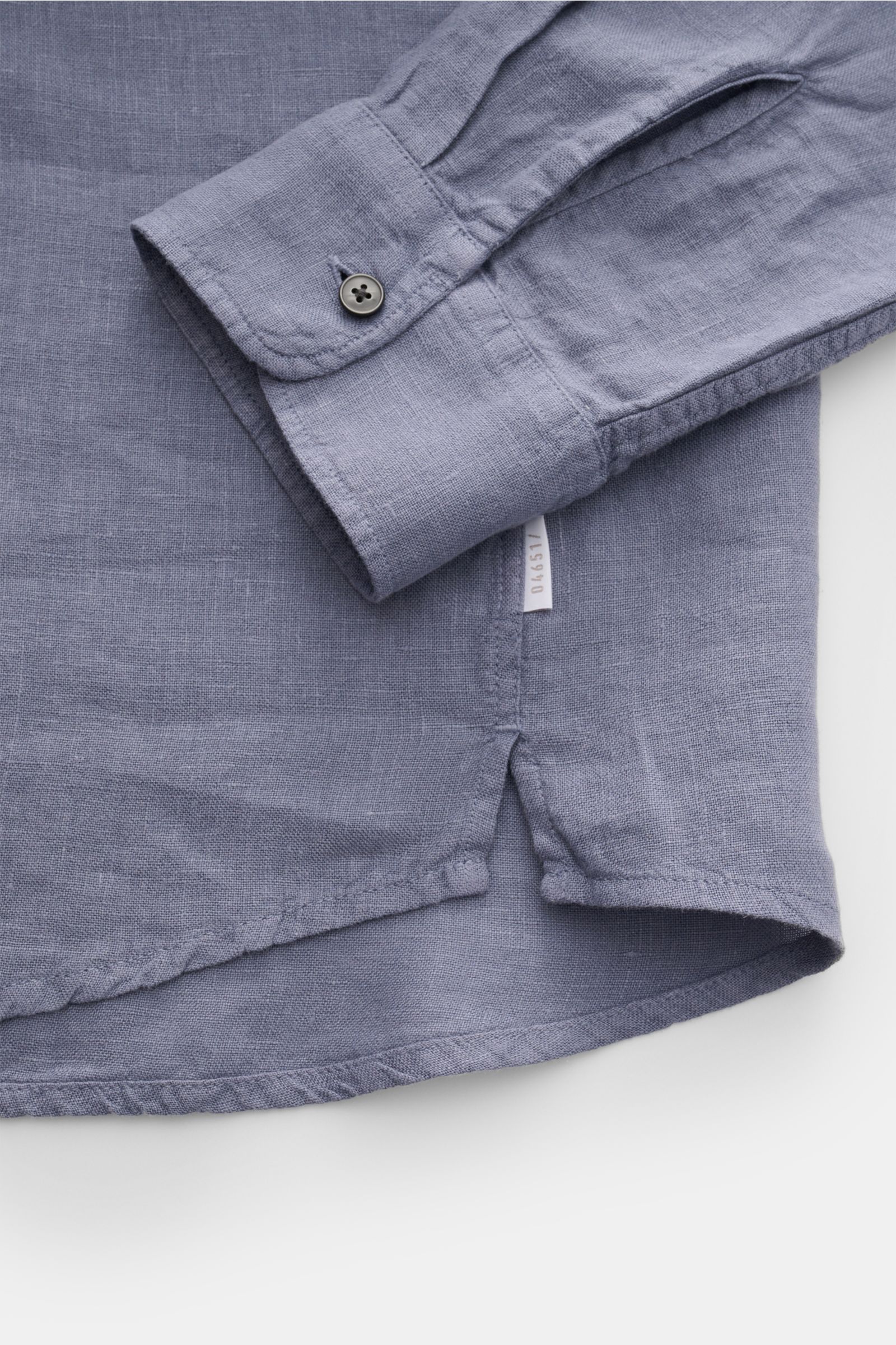 Close-up front-side view of 04651/ A trip in a bag Leinenhemd schmaler Kragen rauchblau showing cuff, side seam with label, and hem details in airy pure linen fabric.

Mühelose Leichtig