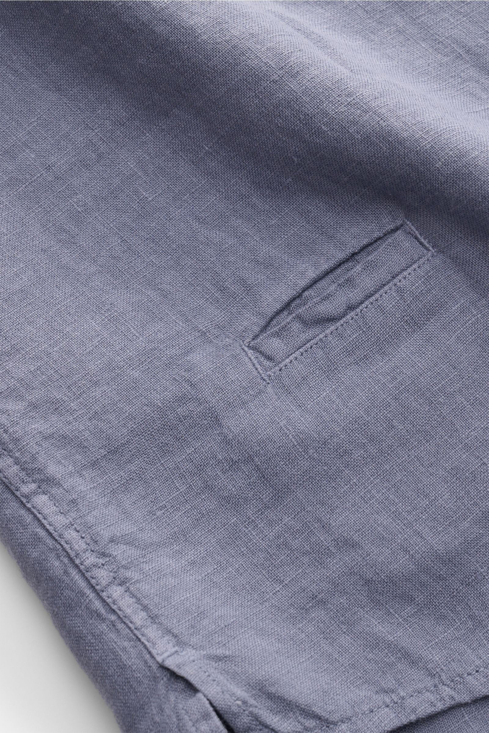 Close-up detail of the lower side hem and side slit of the 04651/ A trip in a bag Leinenhemd schmaler Kragen rauchblau showing the airy pure linen fabric and fine stitching from a top-down perspective. Mühelose 