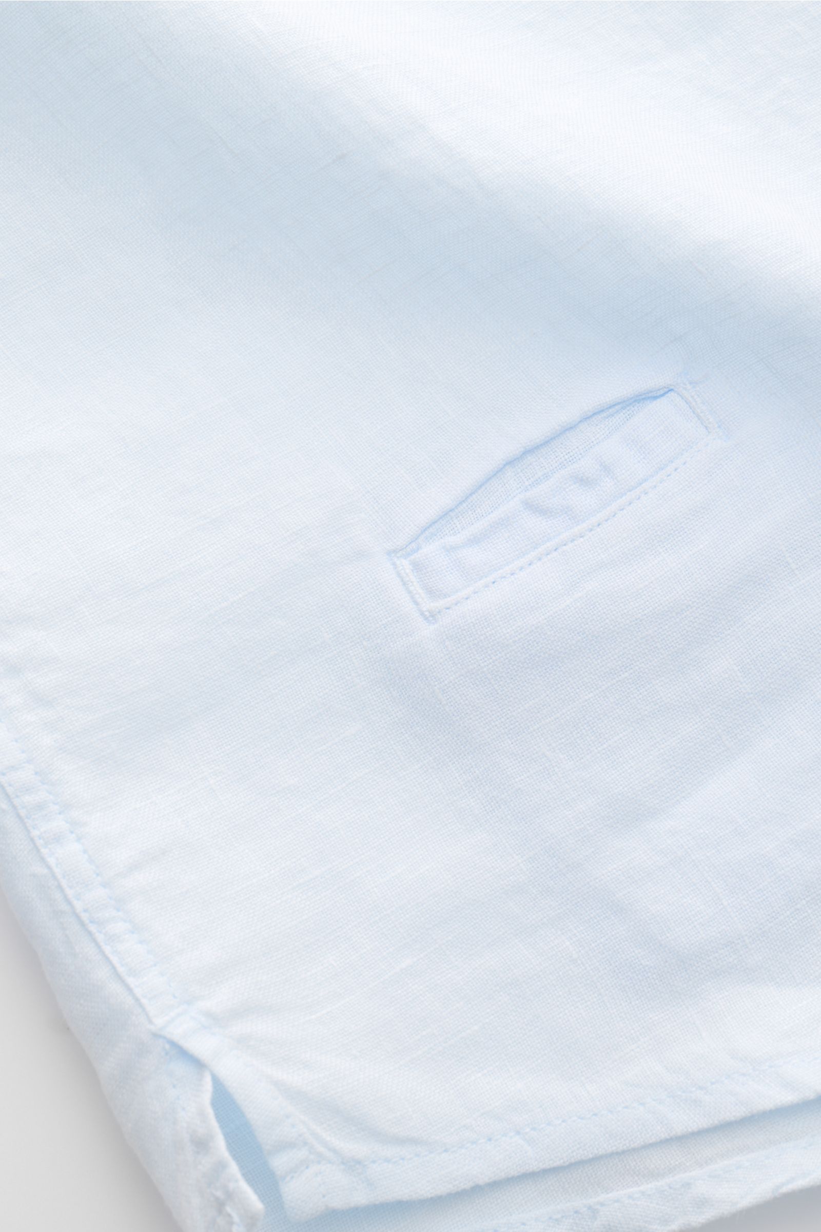 Close-up front-side view of 04651/ A trip in a bag Leinenhemd schmaler Kragen pastellblau showing fabric texture and hem details. Mühelose Leichtigkeit