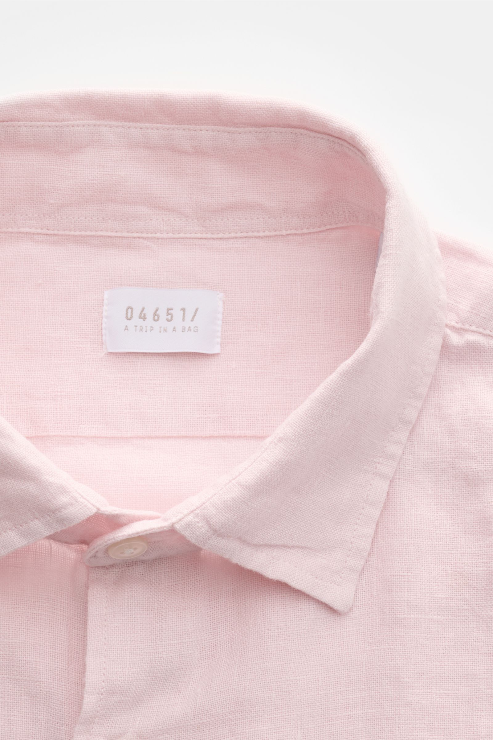 Close-up front view of 04651/ A trip in a bag Leinenhemd schmaler Kragen rosé, a pink linen shirt with a narrow collar and button detail, showcasing the breathable texture and label inside the collar. Mühelose Leichtigkeit: Dieses Hemd aus reinem Leinen v