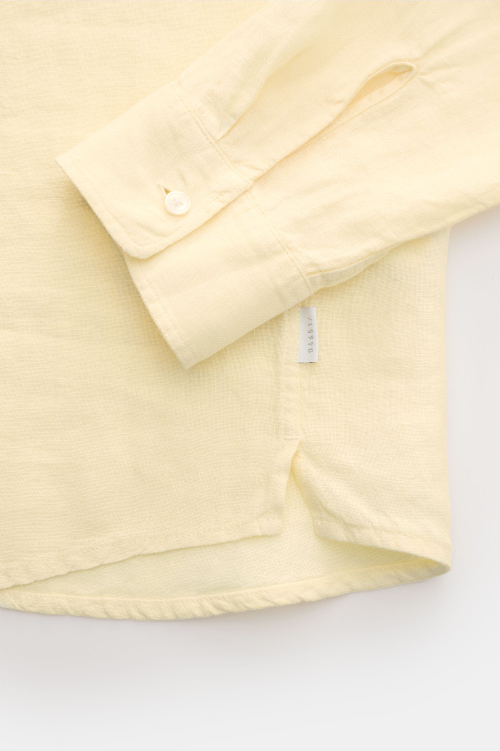 Close-up view of the cuff and hem of the 04651/ A trip in a bag Linen shirt narrow collar pastel yellow, showing pure linen fabric texture, narrow collar, French button placket, classic barrel cuffs, small woven label in the side seam, slightly rounded he