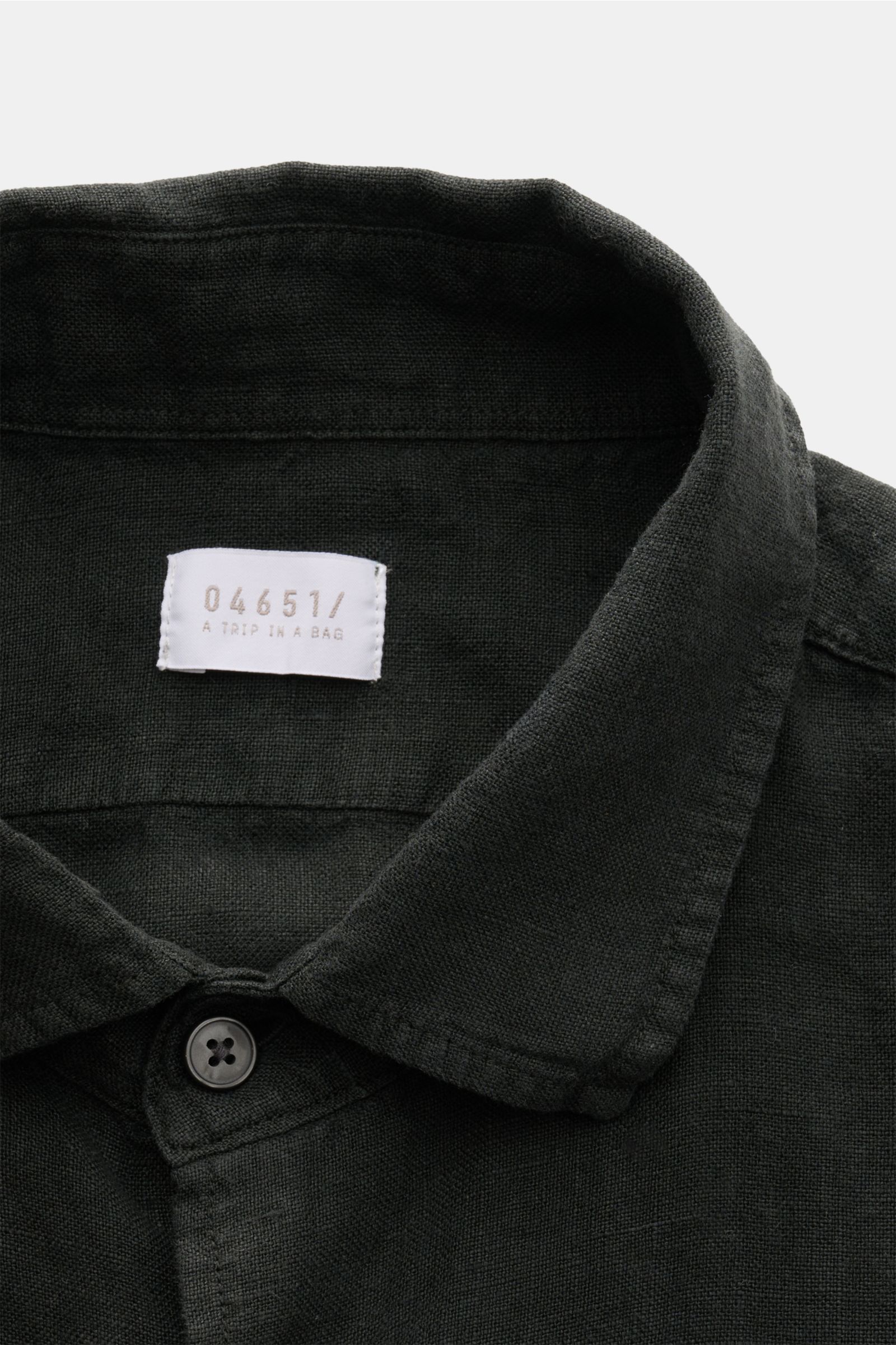 Close-up front view of the black 04651/ A trip in a bag Leinenhemd schmaler Kragen schwarz shirt collar and top button, showing fine linen texture. Mühelose Leichtigkeit