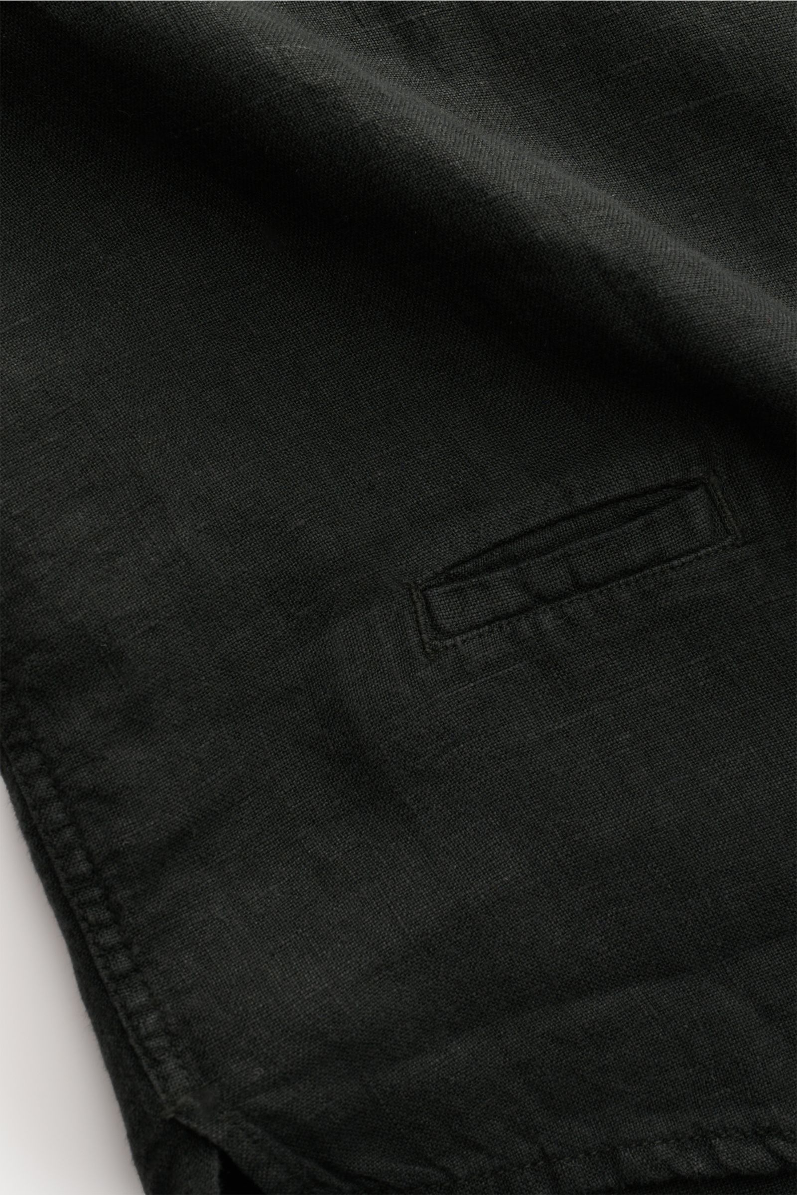 Close-up of the black 04651/ A trip in a bag Leinenhemd schmaler Kragen schwarz showing the fine linen fabric texture and a small side slit from a top angle perspective. Mühelose Leichtigkeit: Dieses Hemd aus reinem Leinen von 04651/ A TRIP IN A BAG überz