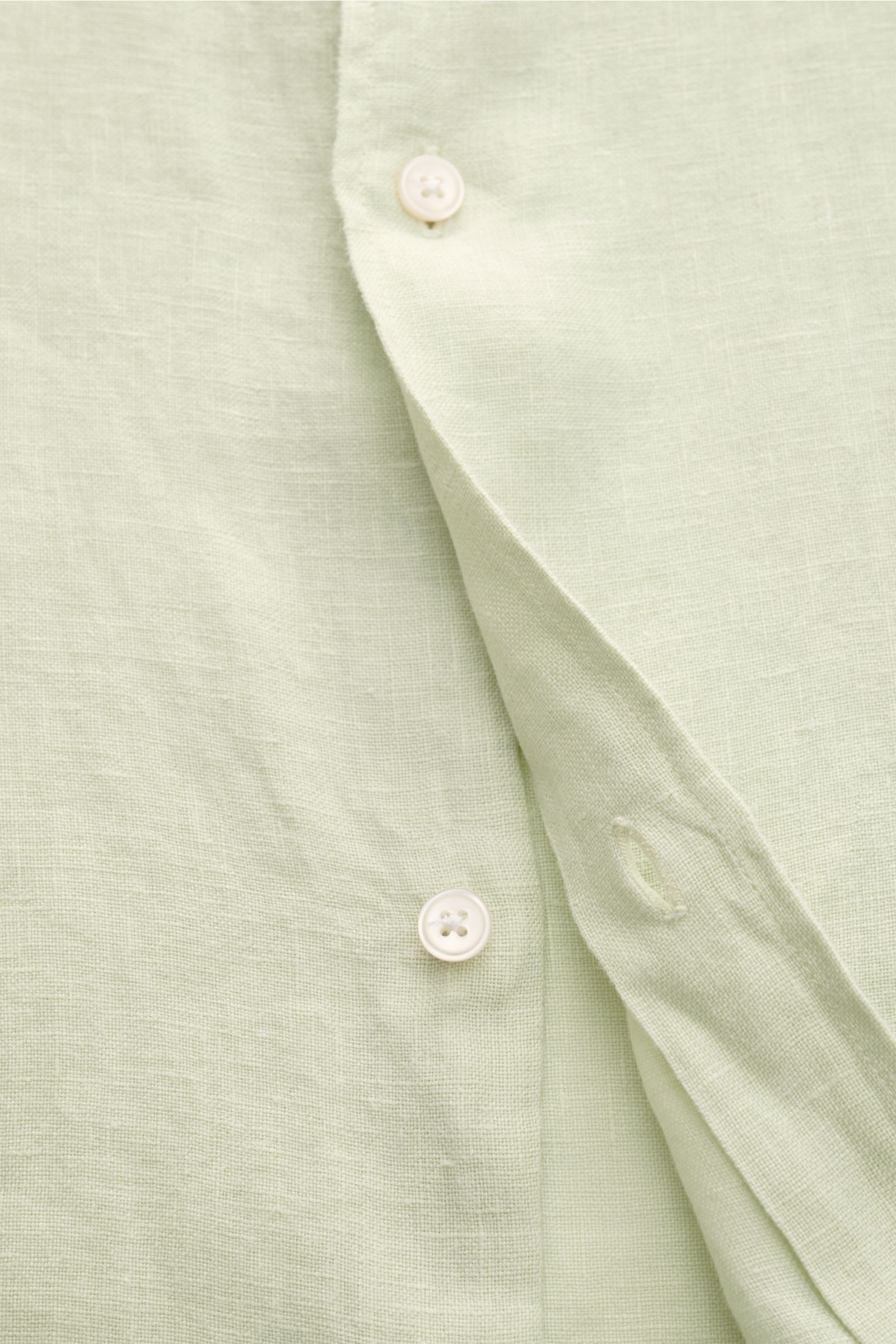 Nahaufnahme des pastellgrünen 04651/ A trip in a bag Leinenhemd 'Linen Guru' mit Grandad-Kragen, reines Leinen, weicher Griff, Regular Fit, französischer Knopfleiste und kleiner Leistentasche, fotografiert von vorne.