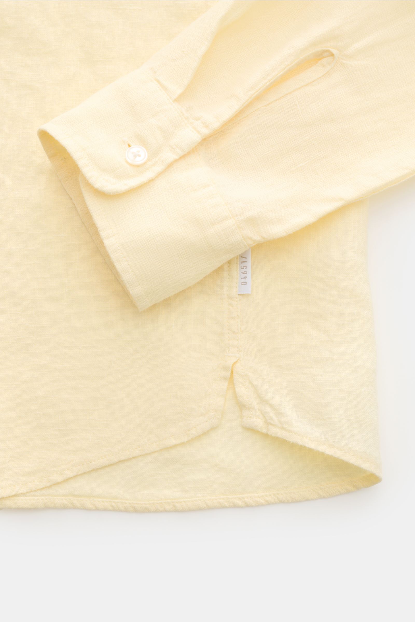 Close-up top-down view of 04651/ A trip in a bag Linen shirt 'Linen Guru' grandad collar pastel yellow showing cuff, small welt pocket, rounded hem, and woven side label, made of pure linen with a soft feel, regular fit, French button placket, classic bar