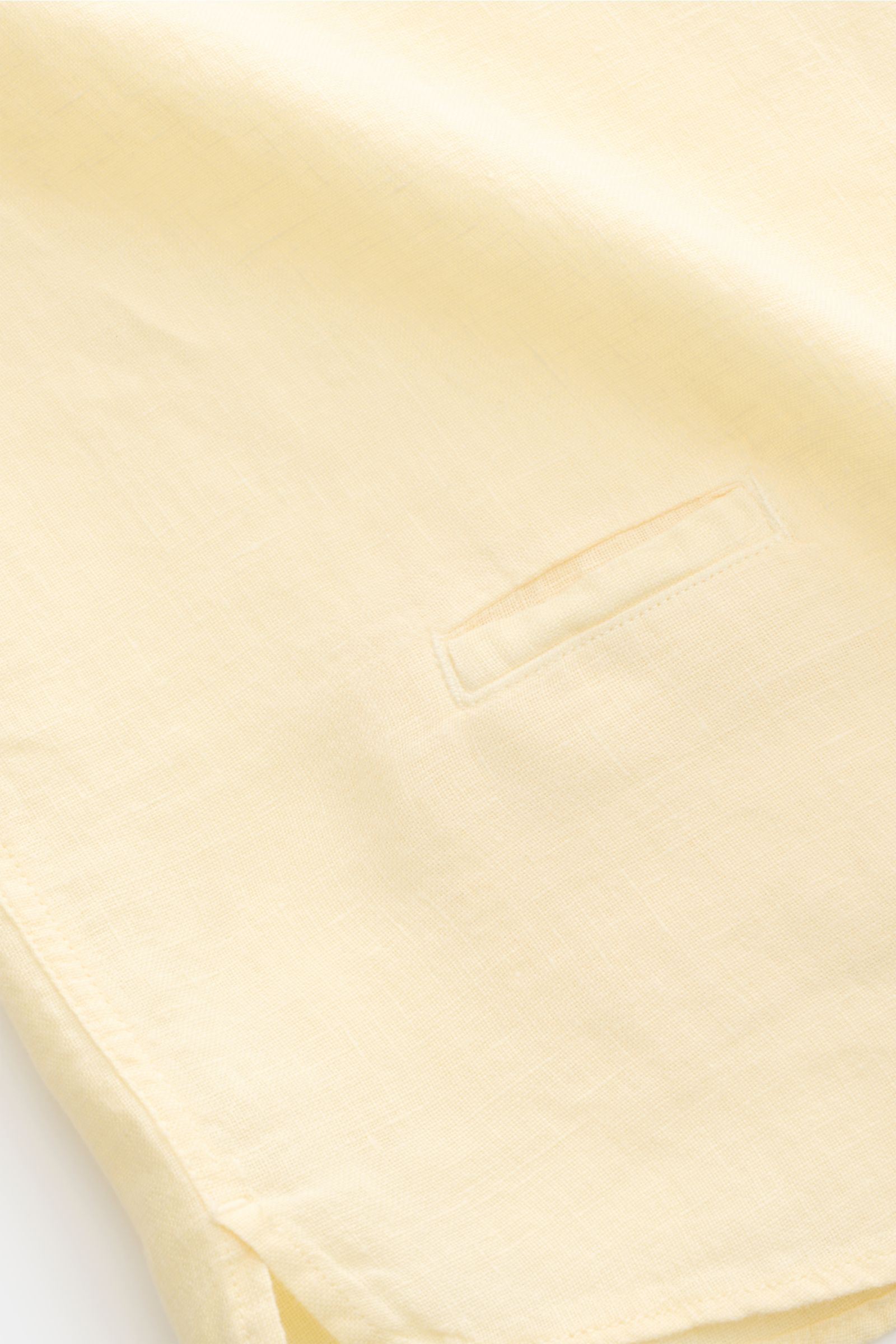 Close-up of the small welt pocket and hem details of the 04651/ A trip in a bag Linen shirt 'Linen Guru' grandad collar pastel yellow, photographed from above. Summer for your skin: The airy casual shirt 'Linen Guru' by 04651/ A TRIP IN A BAG is made of p