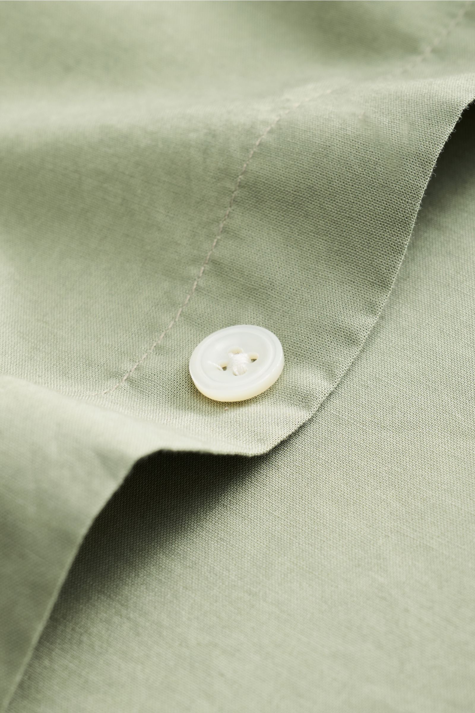 Close-up of a white button on sage fabric of the 04651/ A trip in a bag Casual shirt 'Cloudy Shirt' slim collar sage, photographed from an angled top view.

Lightweight and comfortable for hot days: The casual shirt 'Cloud