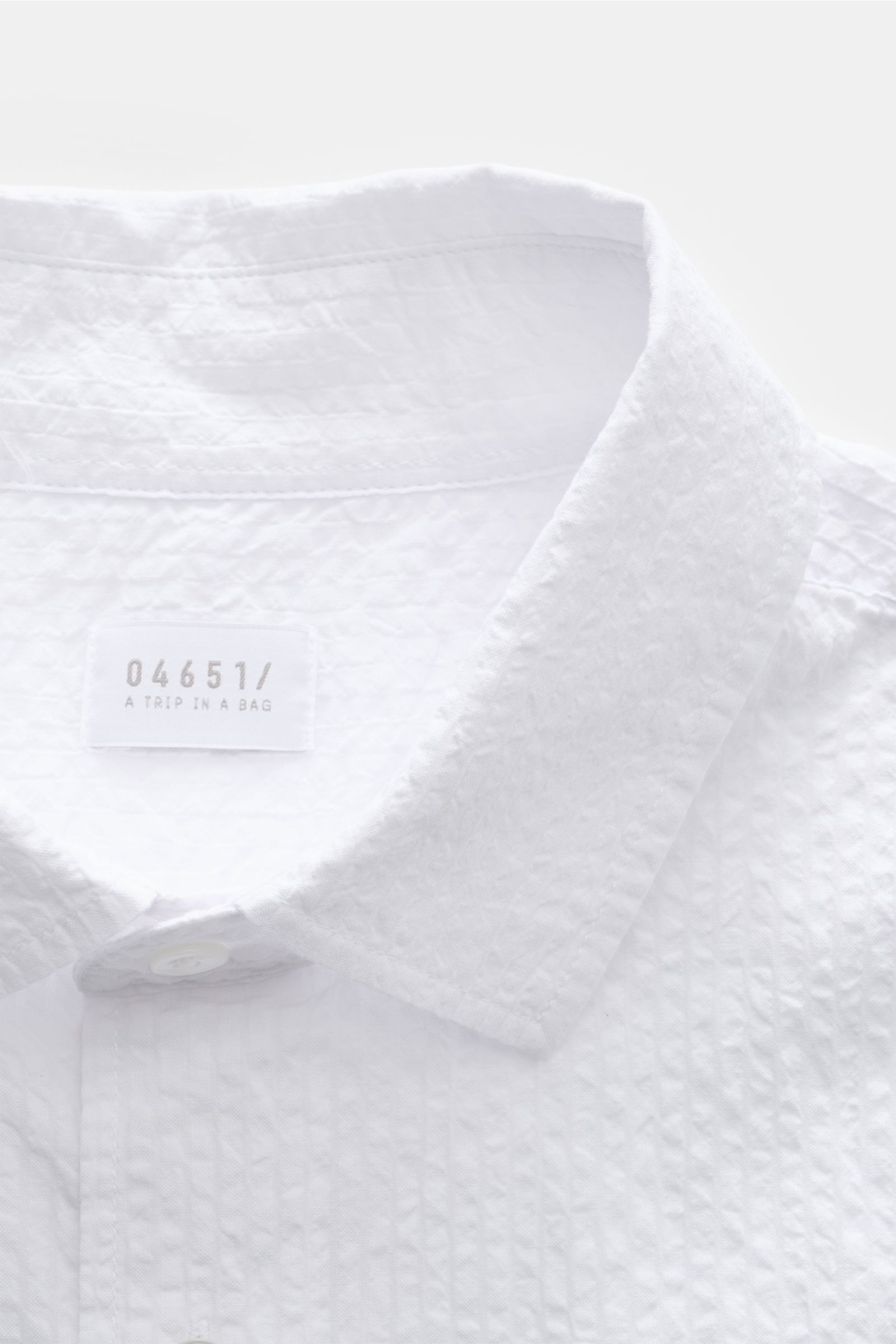 Close-up front view of the 04651/ A trip in a bag Seersucker shirt Kent collar white, showing textured seersucker cotton fabric and label.

Effortlessly casual