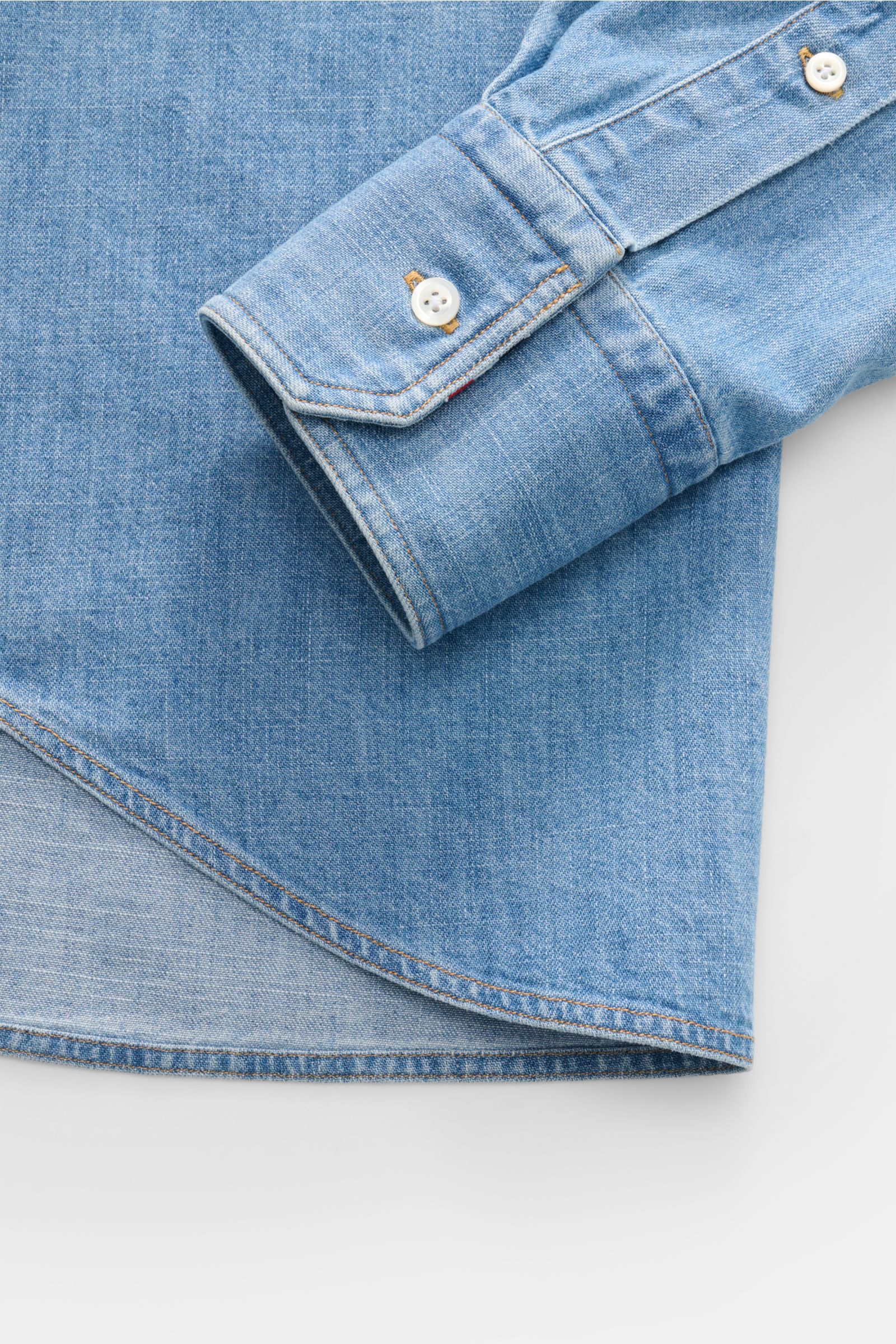 Close-up view of the Thom Browne Jeanshemd Button-Down-Kragen rauchblau sleeve and hem, showing button cuff, light blue cotton fabric, and curved hem.

Description: Zeitlose Luxus-Denimwear: Das Jeanshemd von THOM BROWNE überzeugt mit markentypischen S