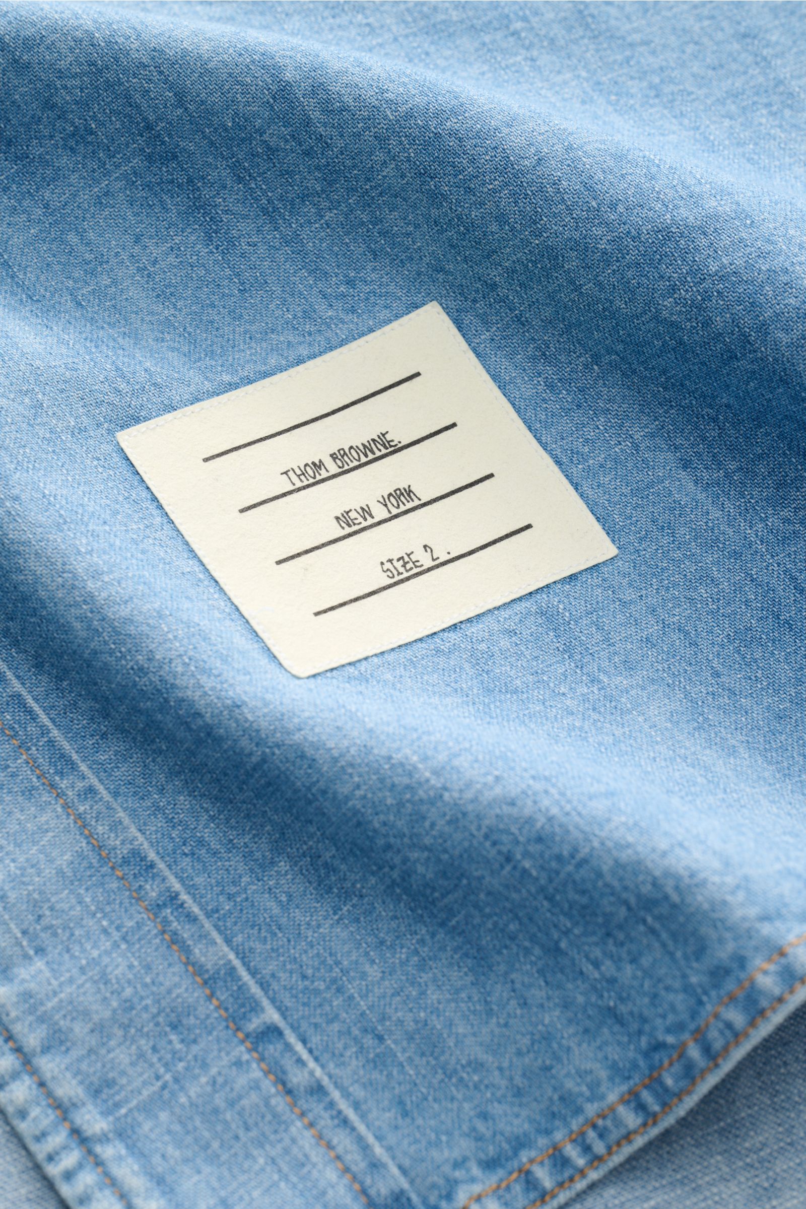 Close-up view of the Thom Browne Jeanshemd Button-Down-Kragen rauchblau showing its fabric texture and brand label.

Zeitlose Luxus-Denimwear: Das Jeanshemd von THOM BROWNE überzeugt mit markentypischen Signature-Elementen und veredelt Casual-Looks mit