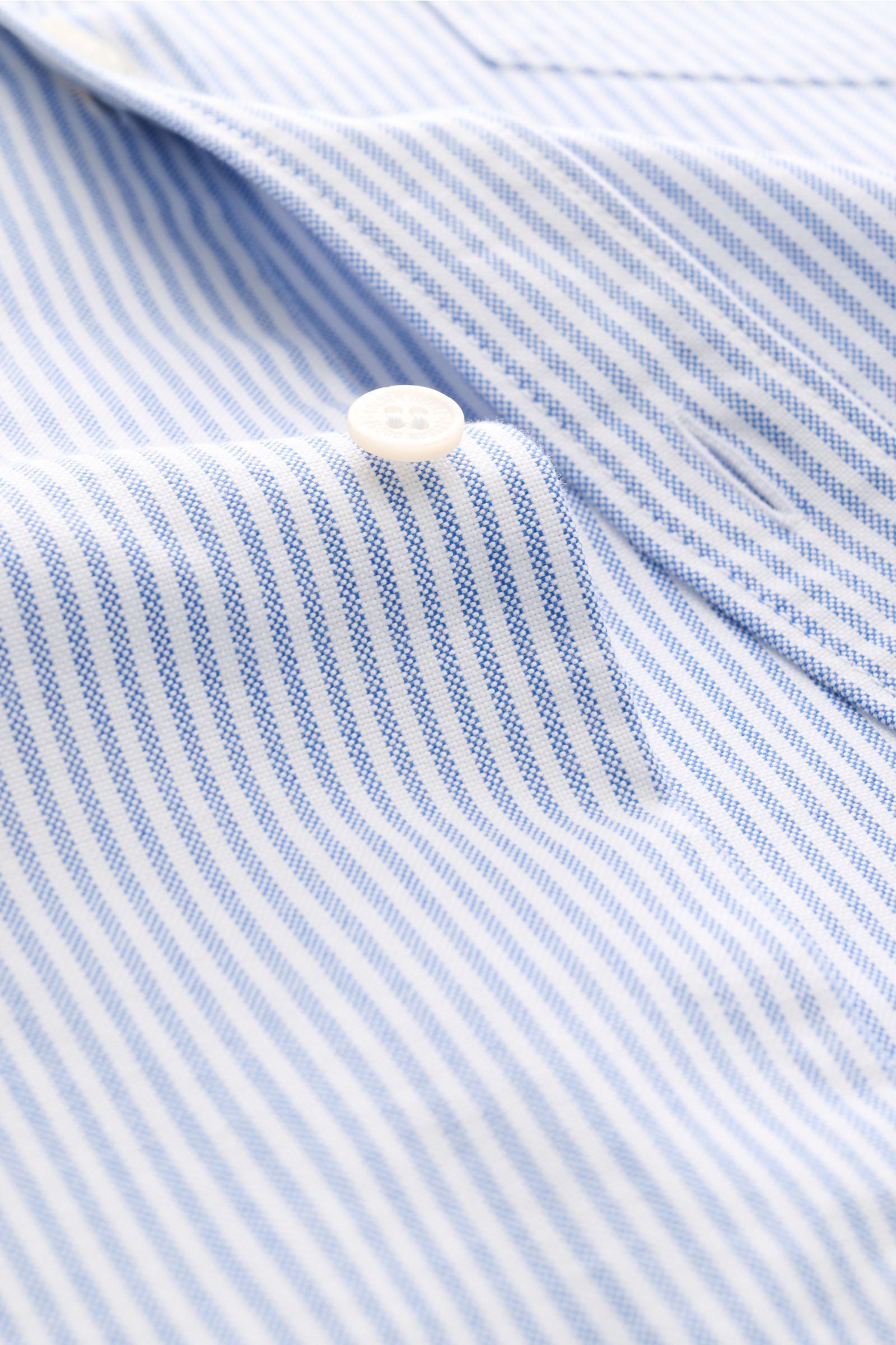 Close-up of blue and white striped fabric with a white button, photographed from an angled top perspective, showing texture and stitching detail of the Golden Goose Oxford-Hemd Kent-Kragen blau/weiß gestreift.

Modernes Essential mit Signature-Attitüde