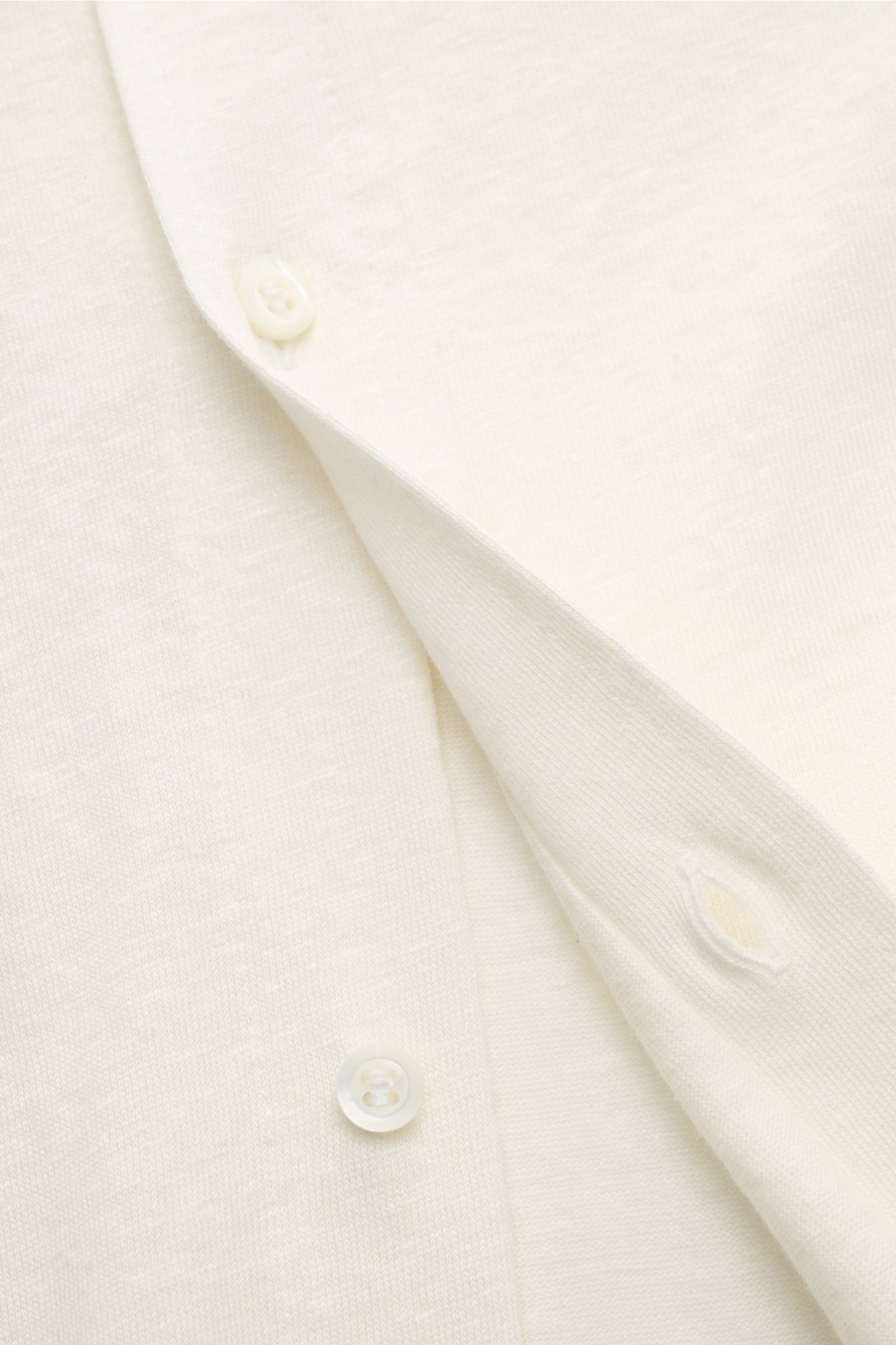 Close-up front view of the cream-colored Brunello Cucinelli Jersey-Hemd Haifisch-Kragen creme, showing soft linen-cotton fabric, button placket, and buttonhole. Zeitlose Raffinesse: Das BRUNELLO CUCINELLI Jersey-Hemd vereint außergewöhnlichen Tragekomfort