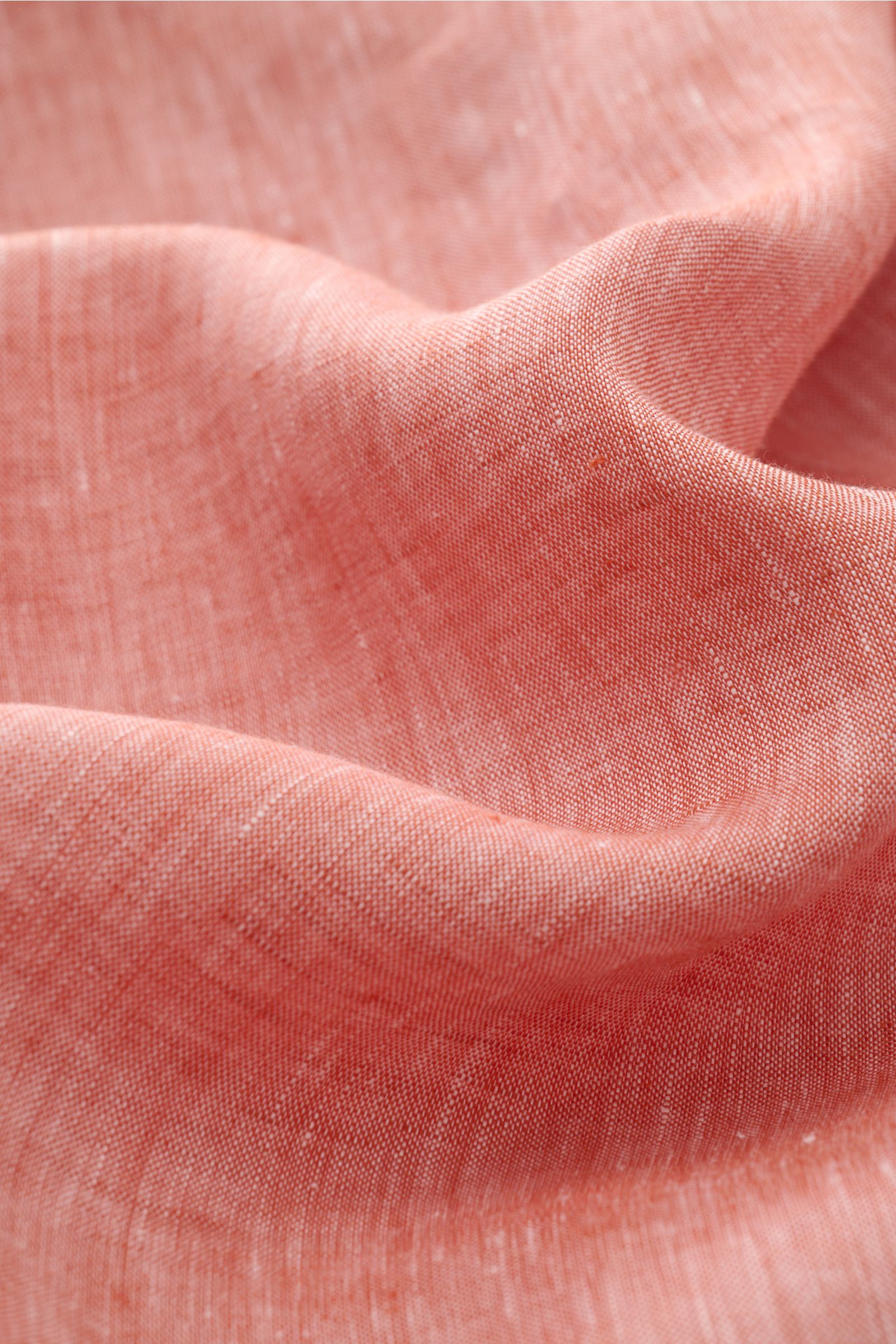 Close-up fabric detail of Brunello Cucinelli Leinenhemd Haifisch-Kragen hellrot meliert, showing light red textured linen material from a top angle. Feinste Leinenqualität: Das sommerlich-leichte Hemd mit Haifischkragen aus dem Hause BRUNELLO CUCINELLI