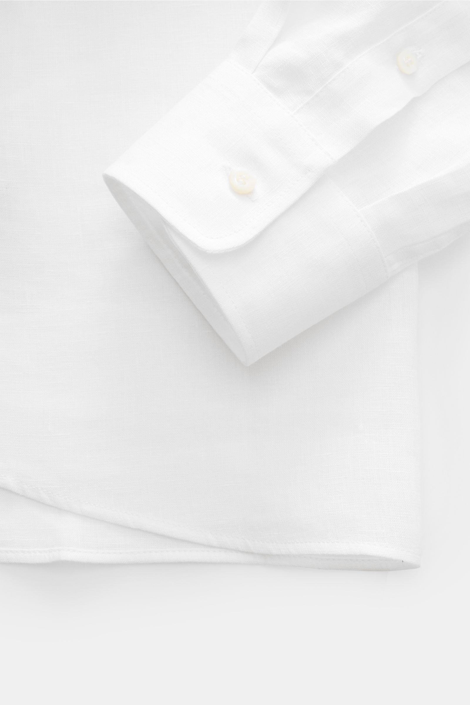 Close-up of the cuff and hem of the Brunello Cucinelli Leinenhemd Haifisch-Kragen weiß, photographed from above, showing pure linen fabric with a regular fit, shark collar, mother-of-pearl buttons on the placket, classic sport cuffs, and a slightly rounde