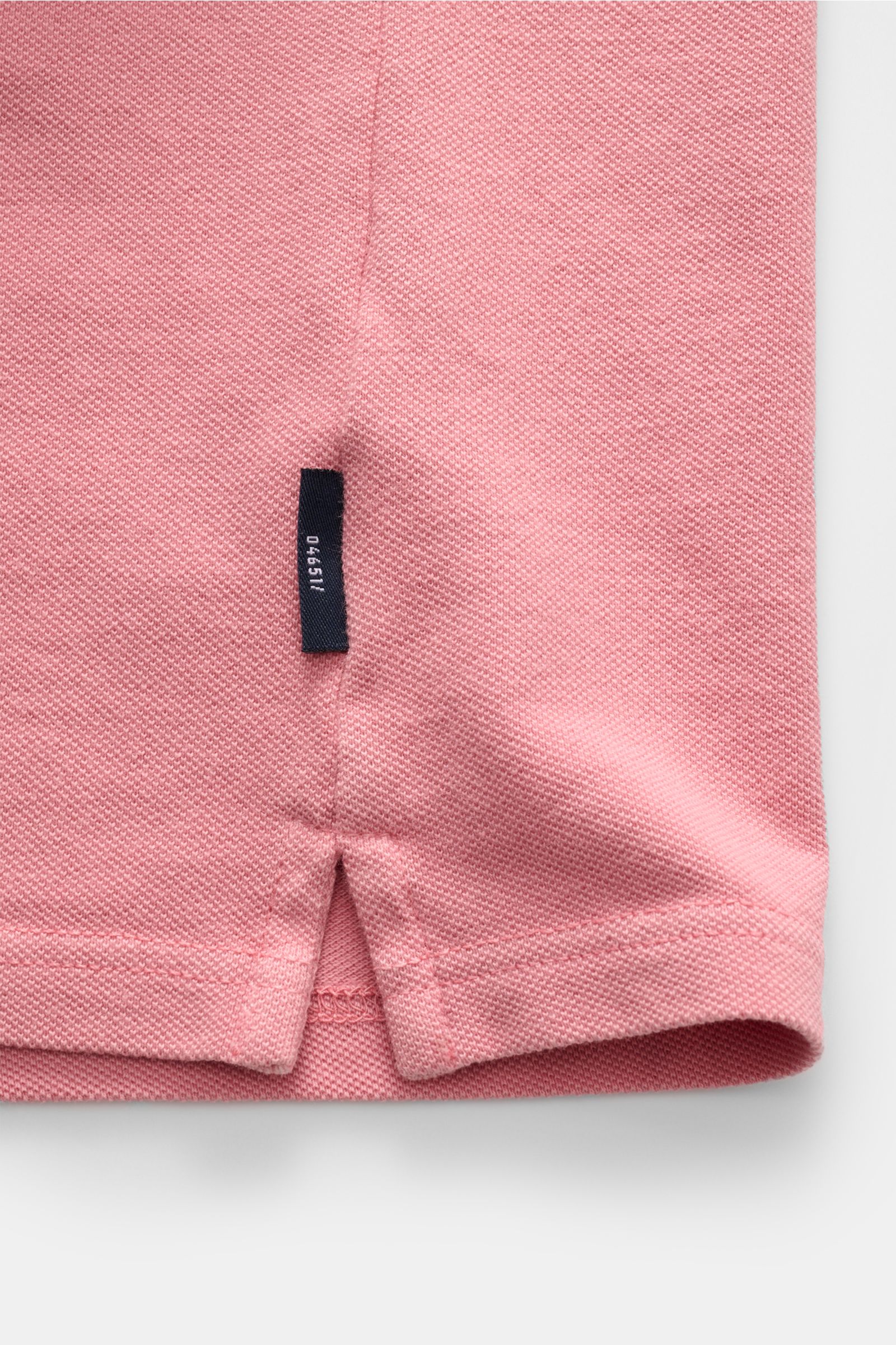 Close-up of pink 04651/ A trip in a bag Hemd Sport shirt hem with black tag, photographed from the side.