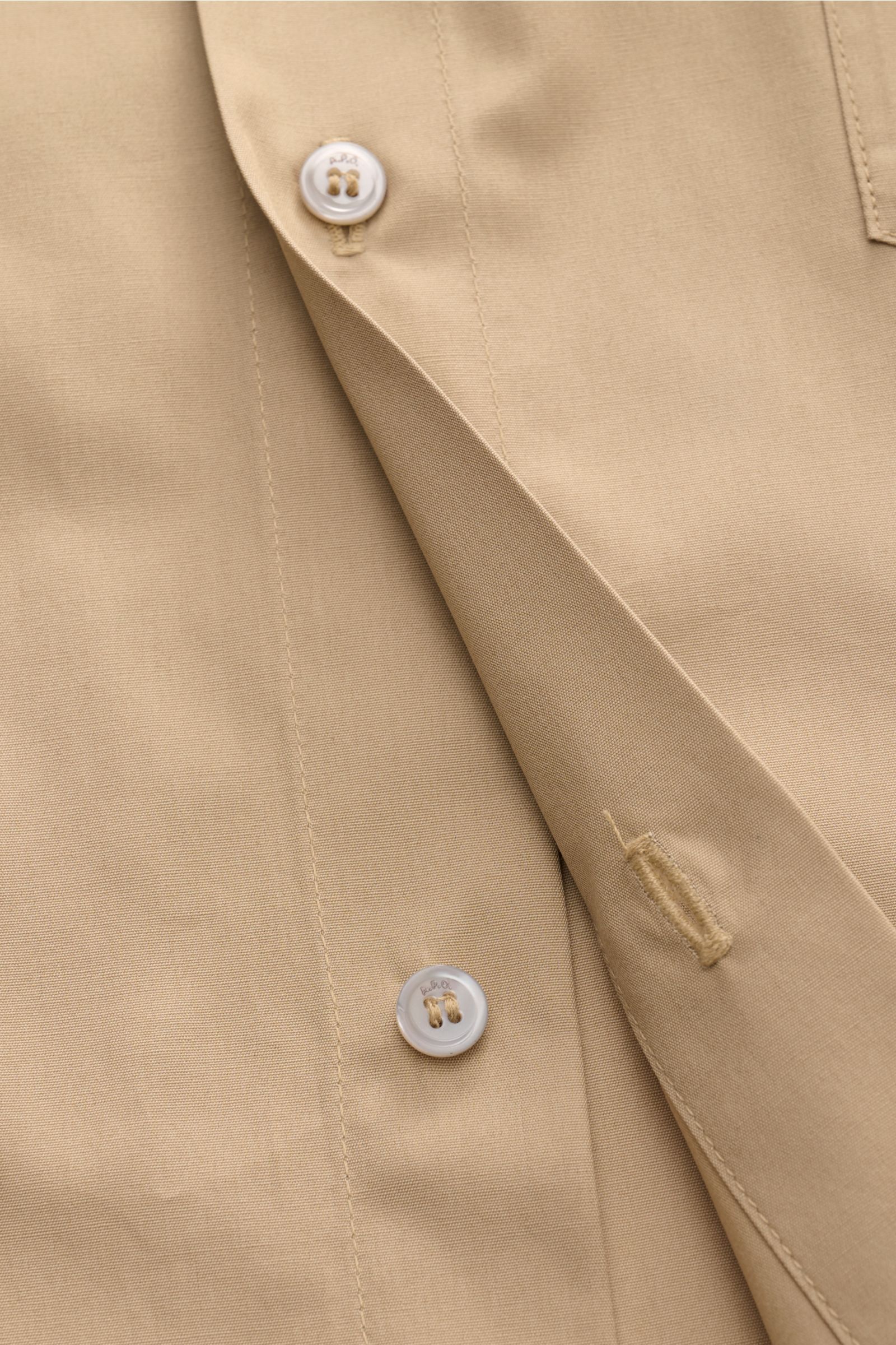 Close-up front detail of A.P.C. Kurzarmhemd Kent-Kragen sand short-sleeve shirt, showing buttons, buttonholes, and smooth cotton fabric.