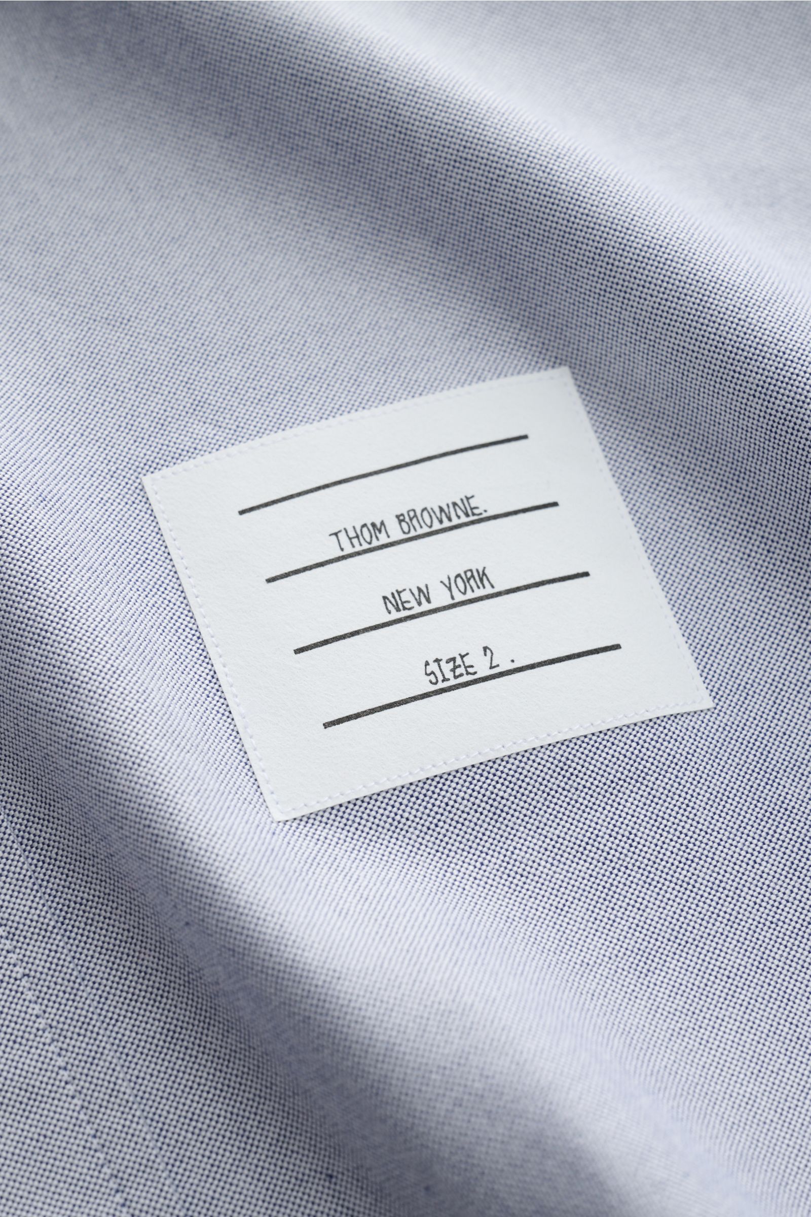 Nahaufnahme des weißen Thom Browne Kurzarmhemd Button-Down-Kragen rauchblau mit Oxford-Baumwolle und Markenlabel, weich fallend.