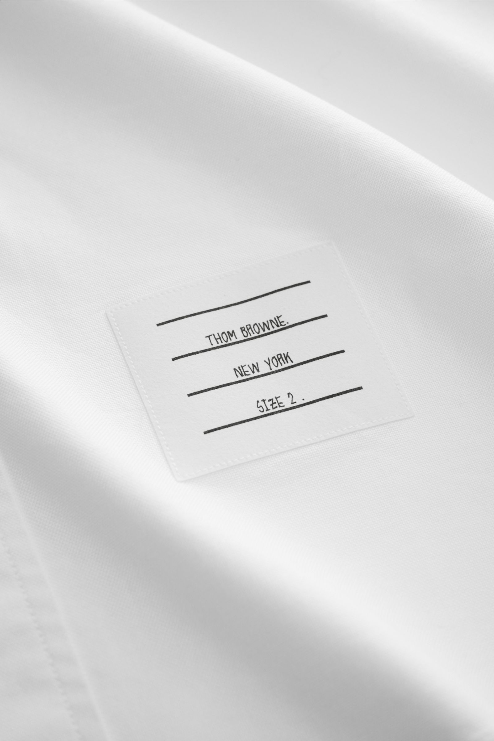 Close-up of the Thom Browne Short-sleeve shirt button-down collar white, showing the label inside on pure cotton Oxford fabric, photographed from a top angle. A modern interpretation of a classic: This stylish short sleeve shirt by THOM BROWNE is a versat