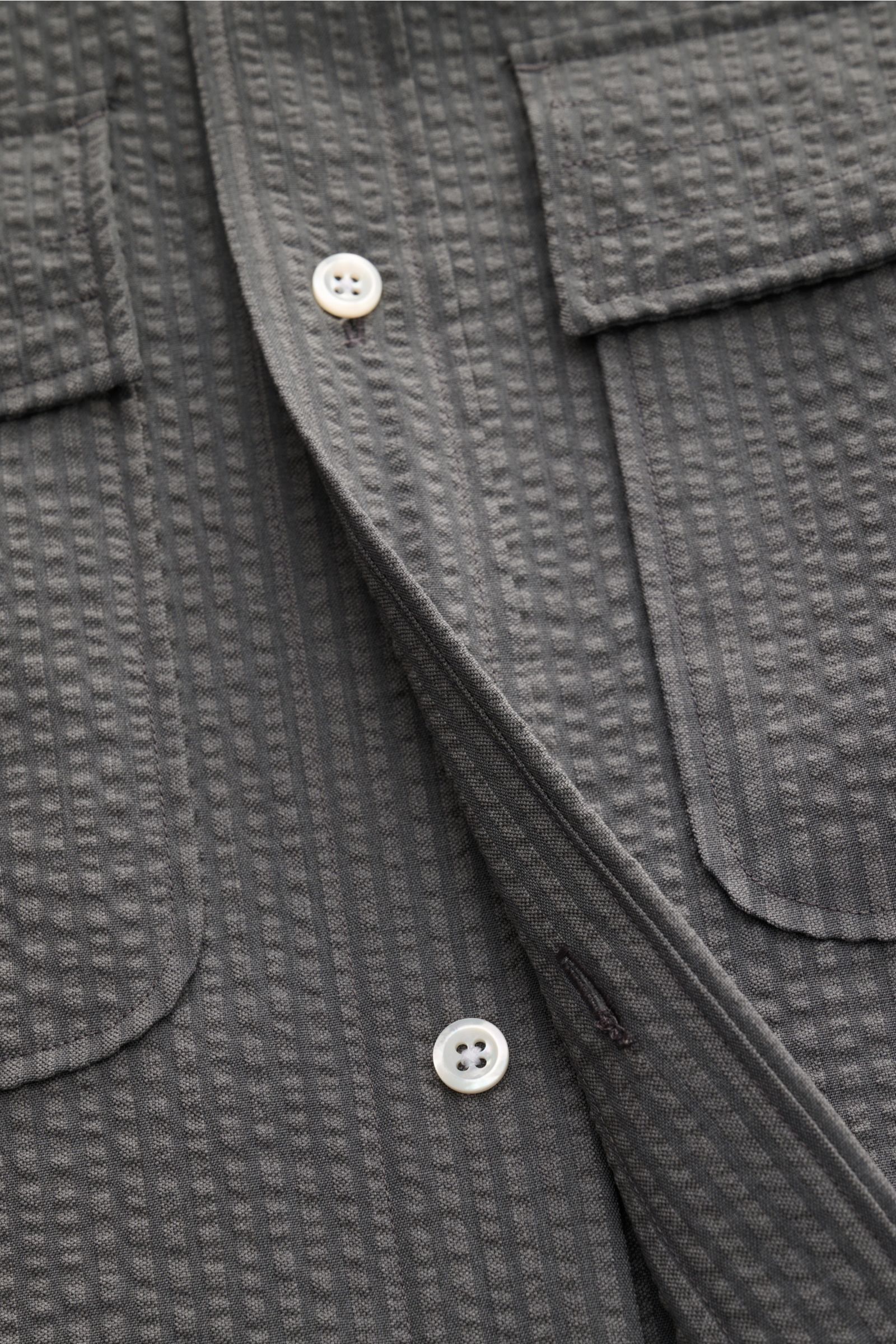 Nahaufnahme des Thom Browne Seersucker-Kurzarmhemd Button-Down-Kragen dunkelgrau mit strukturierter Wollqualität, Perlmuttknöpfen und geknöpften Brusttaschen.