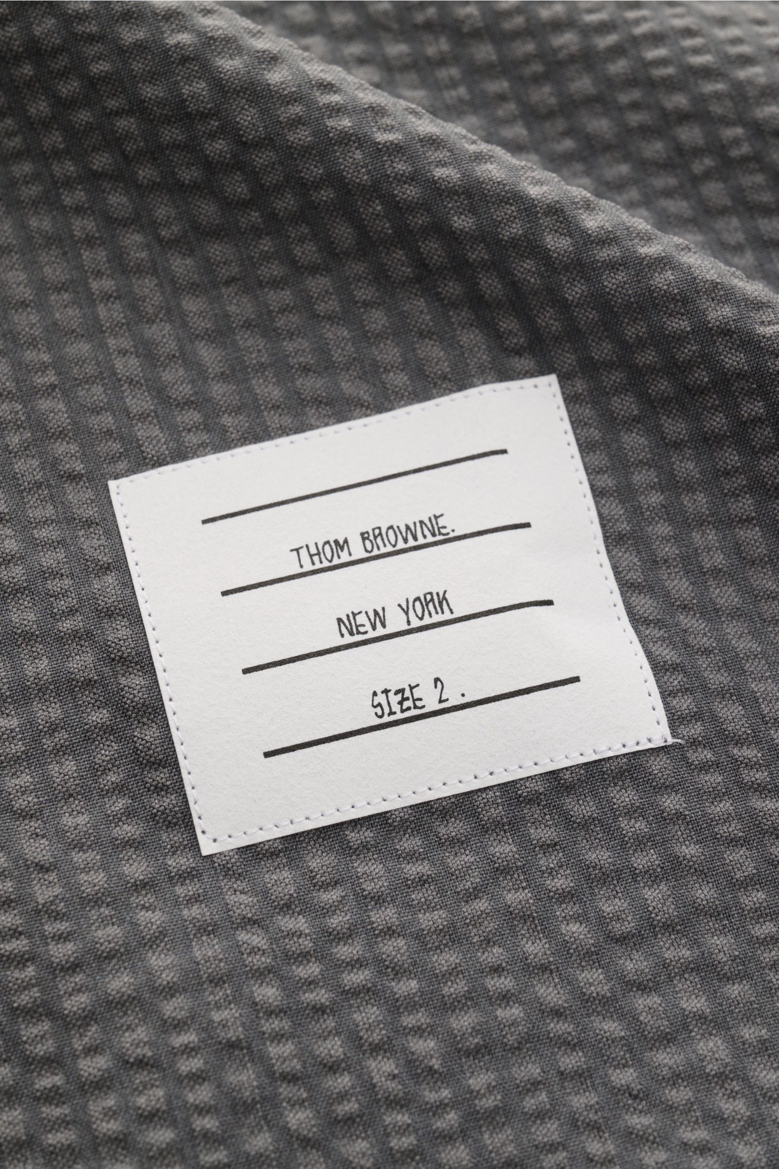 Thom Browne Seersucker-Kurzarmhemd Button-Down-Kragen dunkelgrau Detailaufnahme der strukturierten Wolle mit weißem Markenlabel, Nahaufnahme.