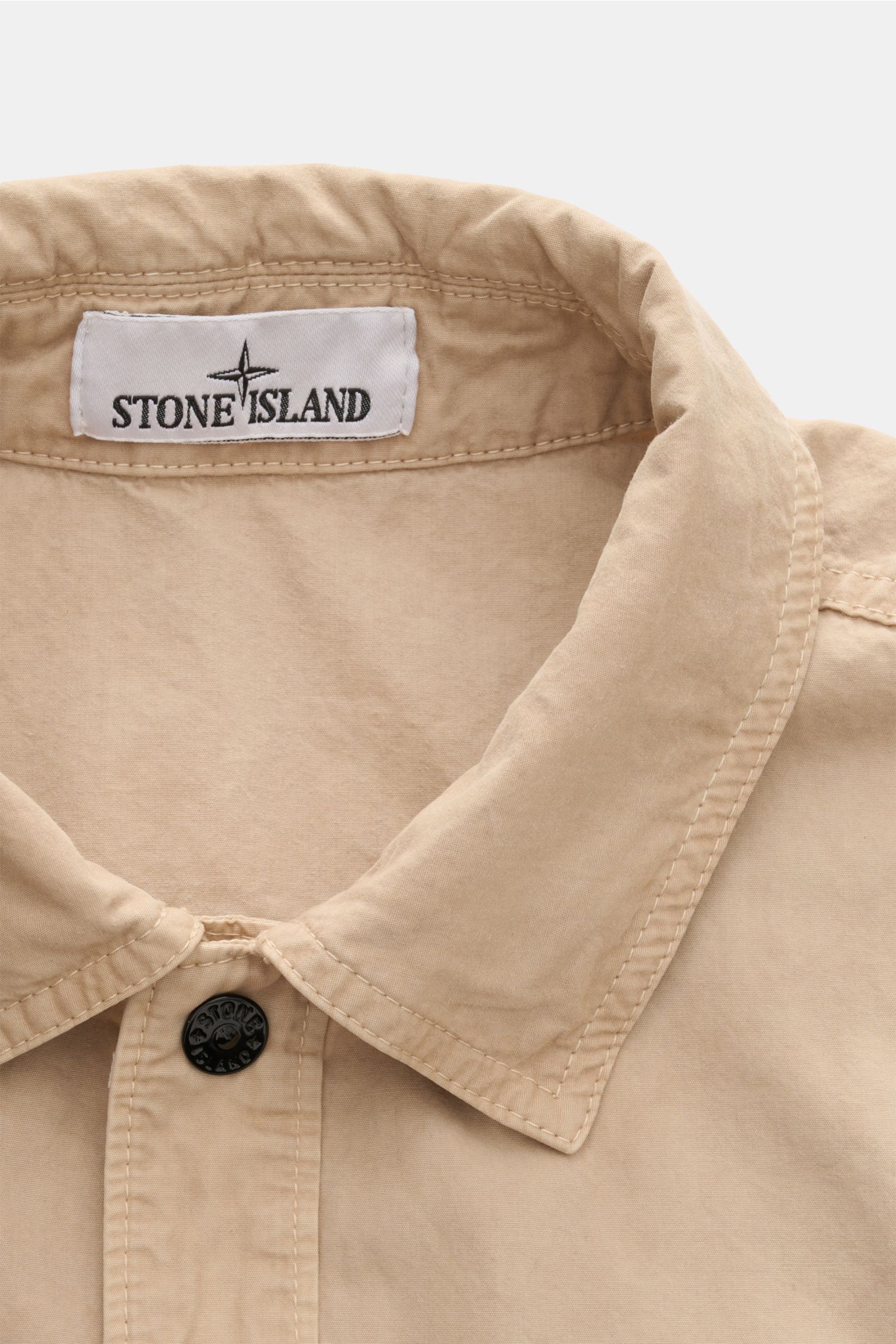 Stone Island Kurzarmhemd 'Brushed Canvas' Kent-Kragen beige, weiche Bio-Baumwolle, Regular Fit, verdeckte Knopfleiste, Brusttasche, Kompass-Badge, Nahaufnahme von oben.