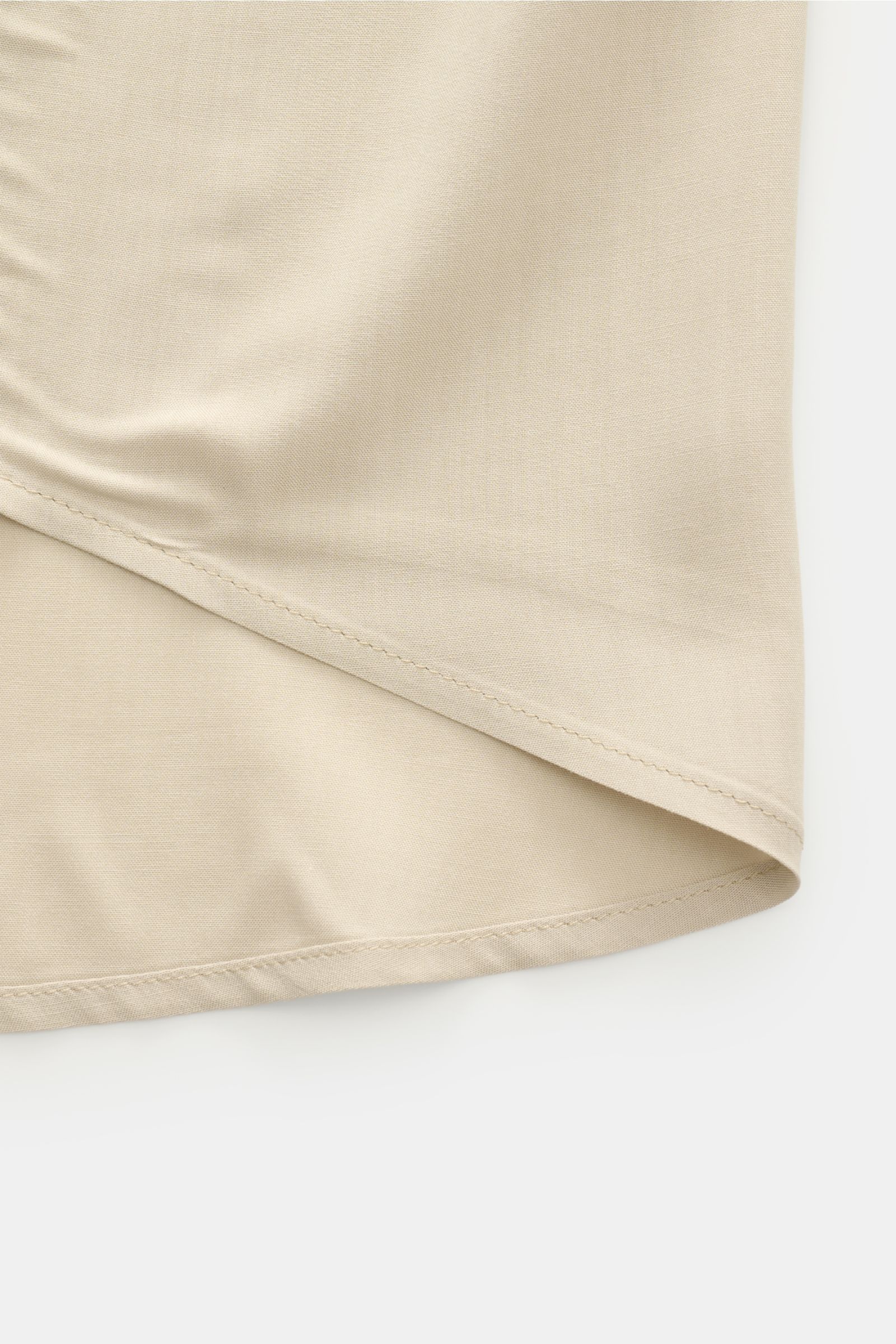 Close-up of the sand-colored Ami Paris Kurzarmhemd 'Boxy' Kubanischer Kragen showing the rounded hemline and smooth fabric texture from a side angle. Modern und lässig: Mit seinem 'Boxy' Fit wird das Kurzarmhemd von AMI PARIS zum unkomplizierten Key-Piece
