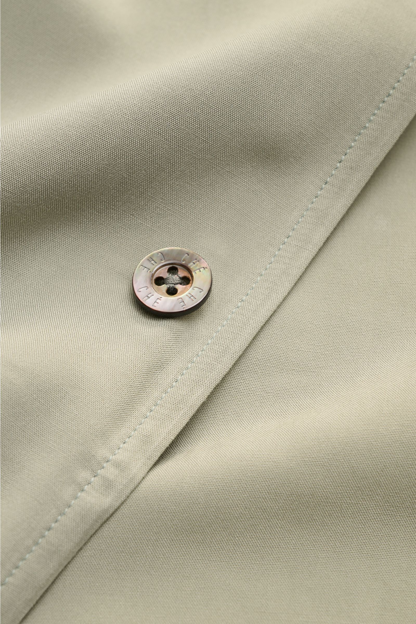 Ché Kurzarmhemd 'Valbonne' Kubanischer Kragen salbei in Nahaufnahme, Knopf mit Logo, weiche Viskose, Oversized Fit, Kontrastdetails innen.