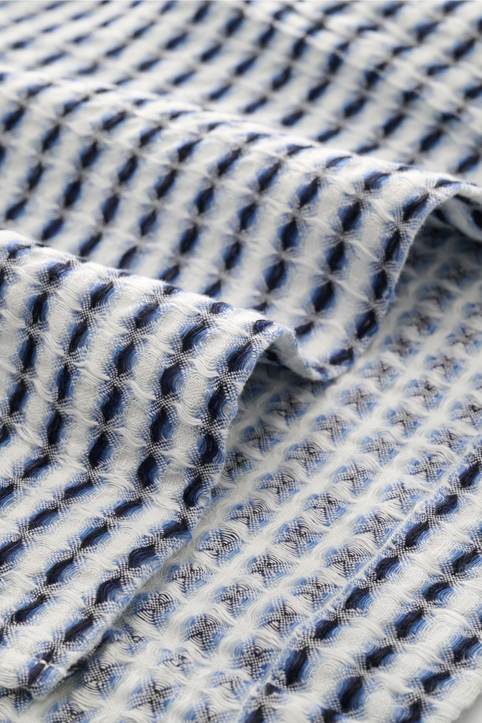 Close-up angled view of the woven blue and white waffle pique fabric of the Ché Leinen-Kurzarmhemd 'Riita' Kubanischer Kragen blau/weiß gemustert, showcasing its coarse, airy knit and textured linen material.

Description: Im Sommer kreiert das Leinen-