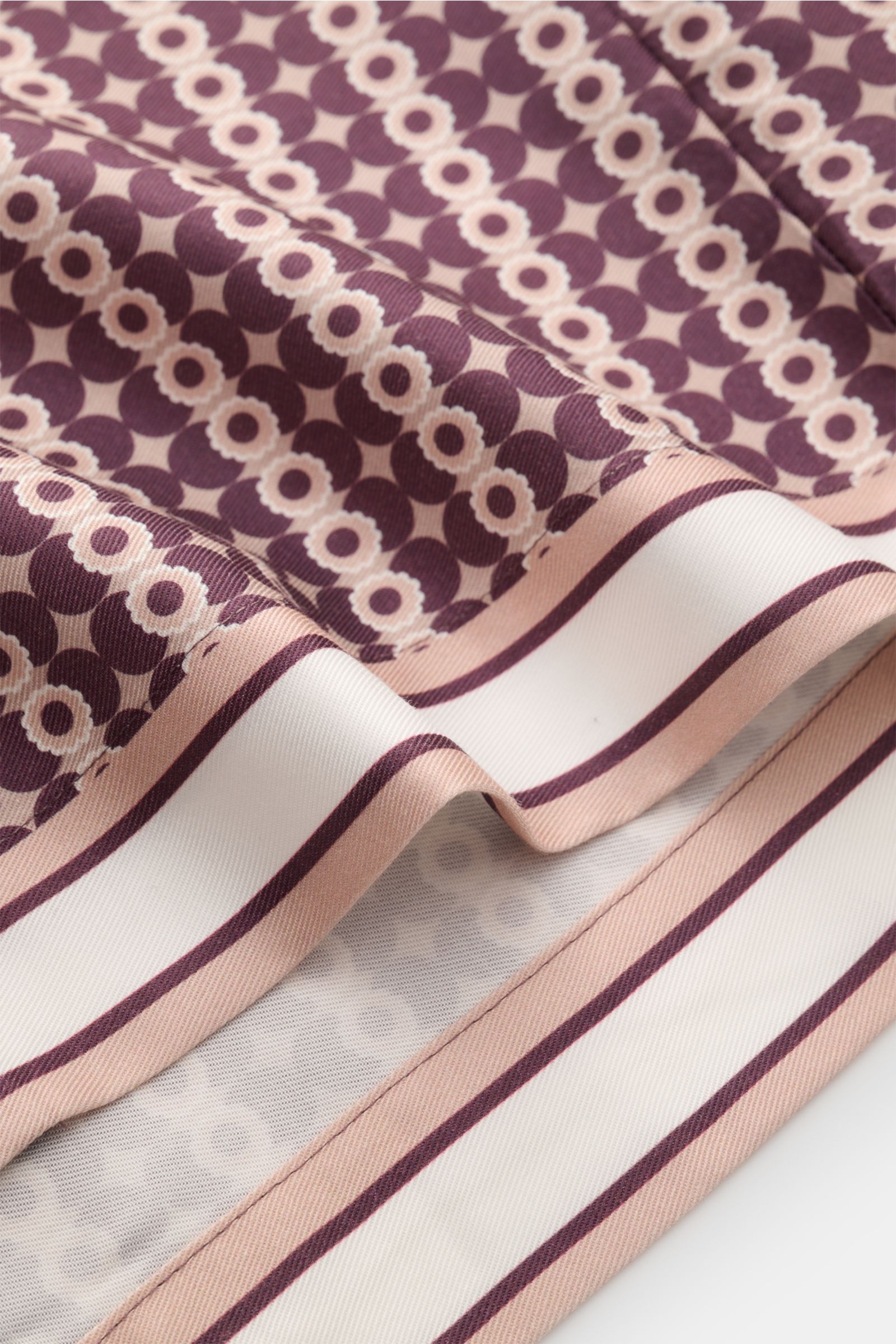 Nahaufnahme des Ché Kurzarmhemds 'Pressoa' Kubanischer Kragen bordeaux/hellbraun gemustert, Stoff mit ornamentalem Muster, Lyocell, glatter Griff, seitlicher Saumschlitz, gerader Saum, fotografiert aus seitlicher Perspektive.