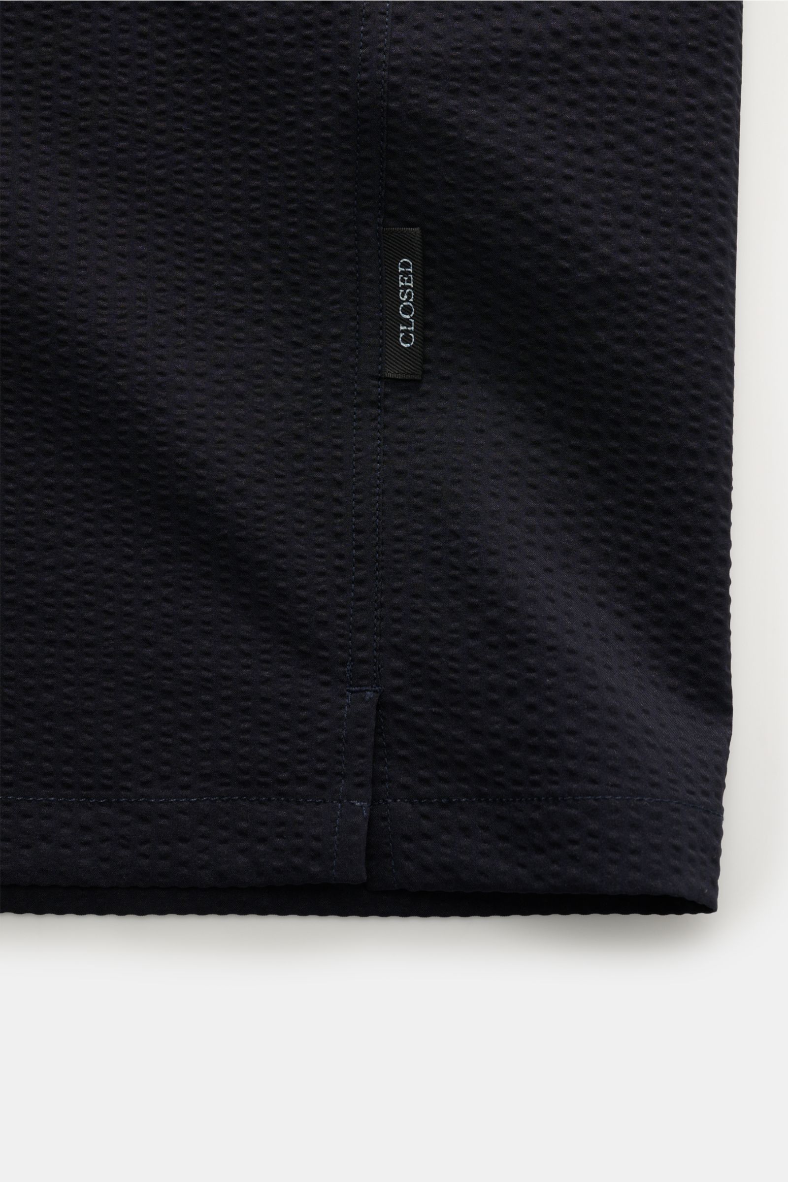 Nahaufnahme des Closed Kurzarmhemd Kubanischer Kragen dark navy in Seersucker-Optik mit Label, leichte Struktur und feine Nähte, seitlicher Blick.