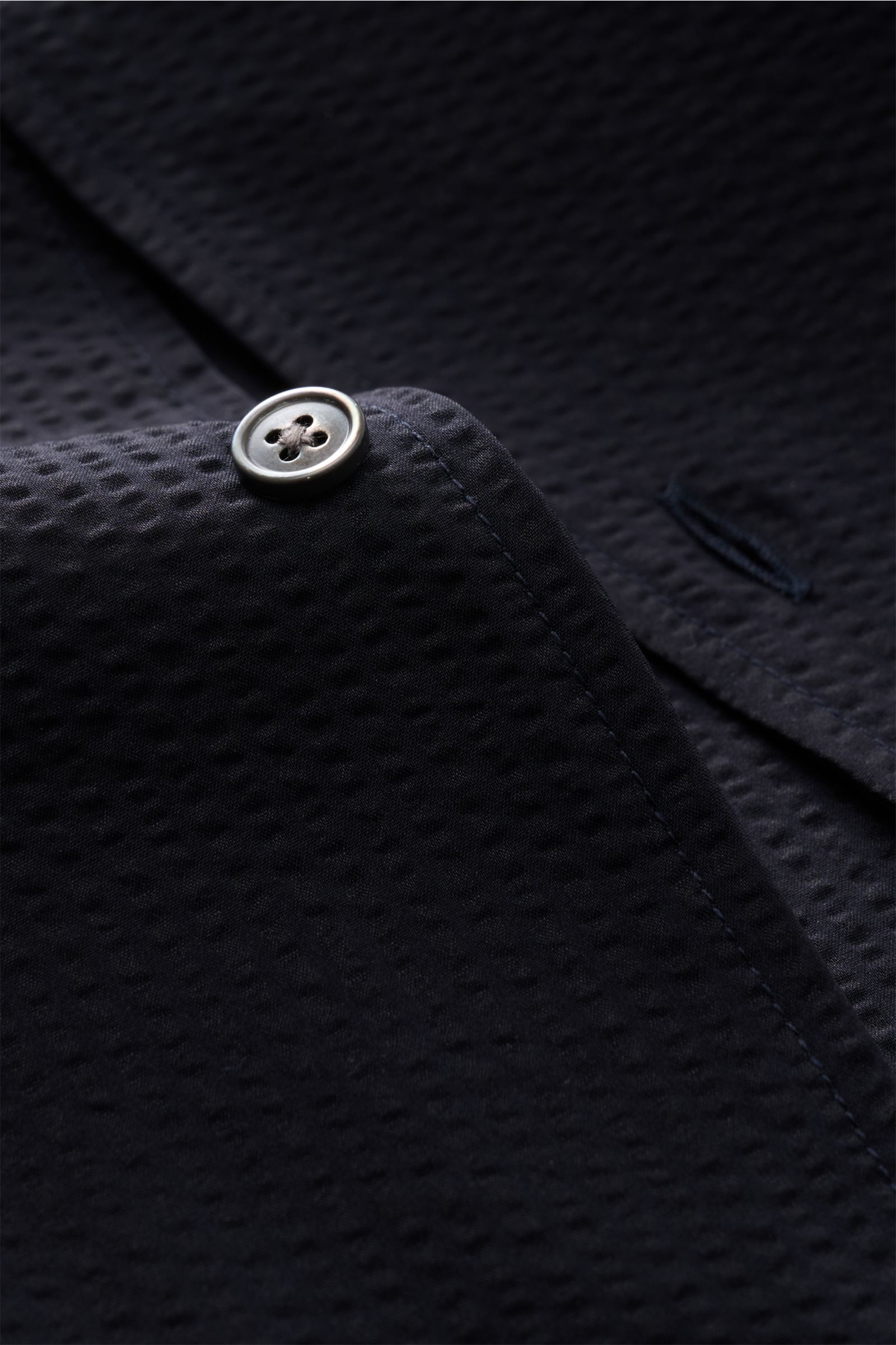 Nahaufnahme des Closed Kurzarmhemd Kubanischer Kragen dark navy in Seersucker-Optik, Fokus auf Knopf und strukturierte Microfaser.