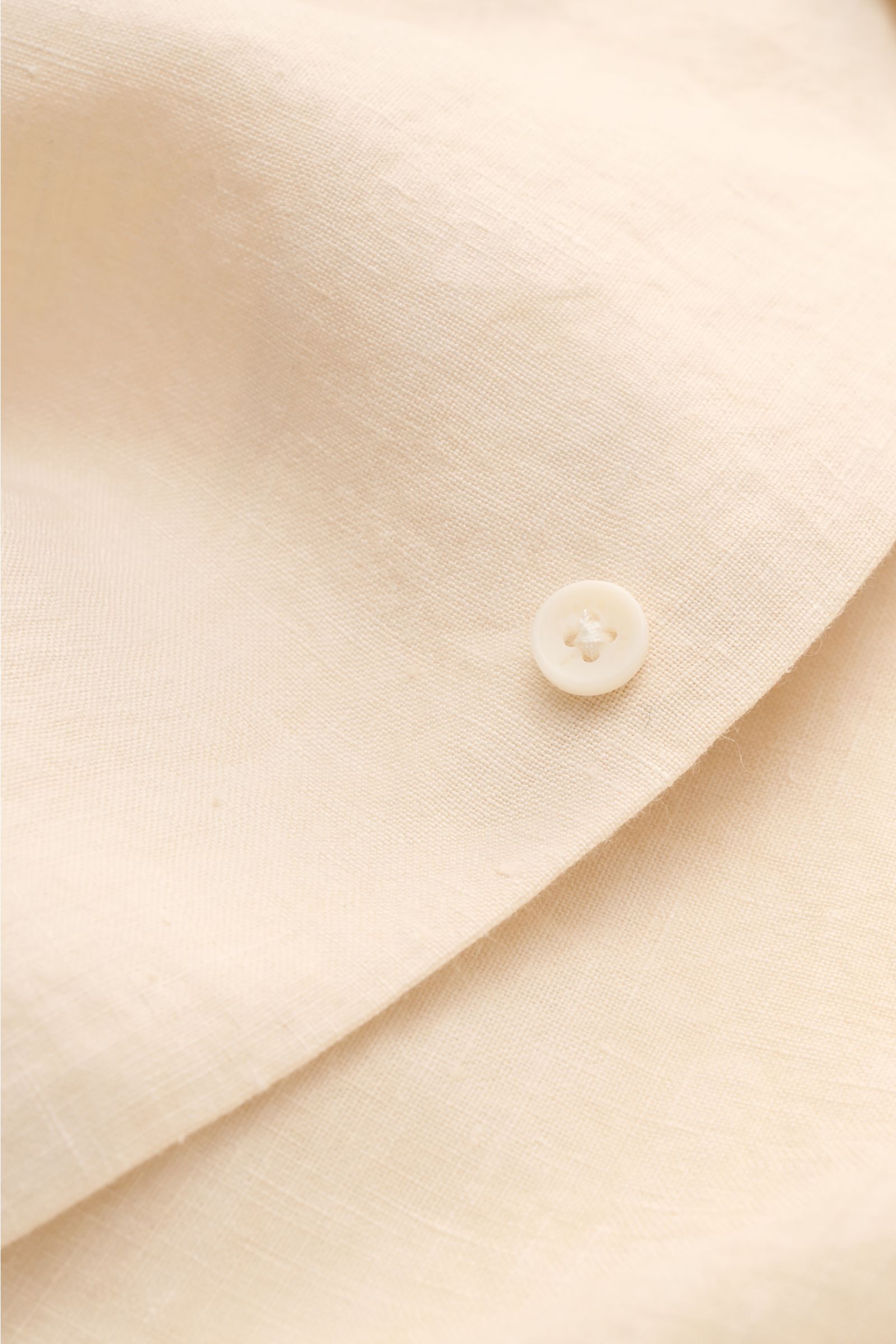 Close-up front view of the Percival Linen short sleeve shirt Cuban collar beige focusing on the fabric texture and button. Cool, lightweight and antibacterial: Linen’s natural qualities make it the perfect summer material. PERCIVAL has chosen the sustaina