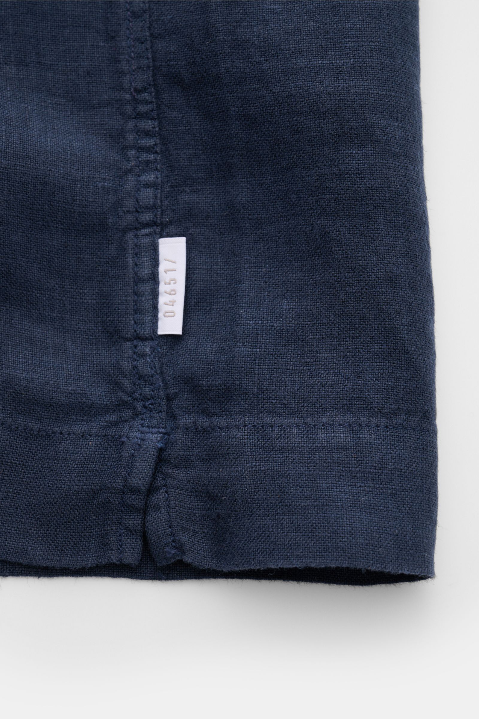 Nahaufnahme des Saumabschnitts mit kleinem Weblabel der 04651/ A trip in a bag Leinen-Kurzarmhemd Kubanischer Kragen navy aus reinem Leinen.