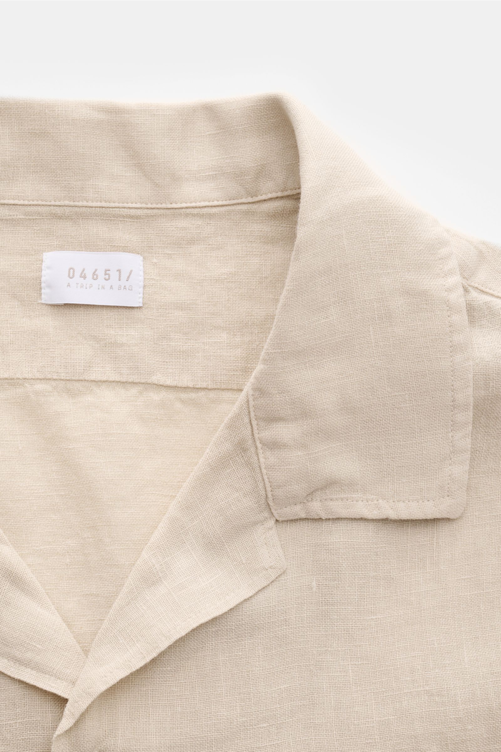 Detailaufnahme des beigen 04651/ A trip in a bag Leinen-Kurzarmhemd Kubanischer Kragen aus reiner Leinenqualität mit französischer Knopfleiste und feiner Struktur.