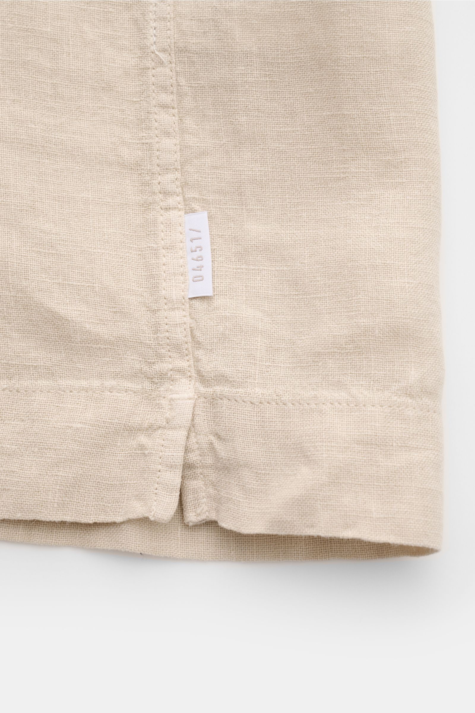 Beige Detailaufnahme des Saumverlaufs mit kurzem Schlitz und kleinem weißen Weblabel des 04651/ A trip in a bag Leinen-Kurzarmhemd Kubanischer Kragen, aus reinem Leinen, luftiger Qualität.