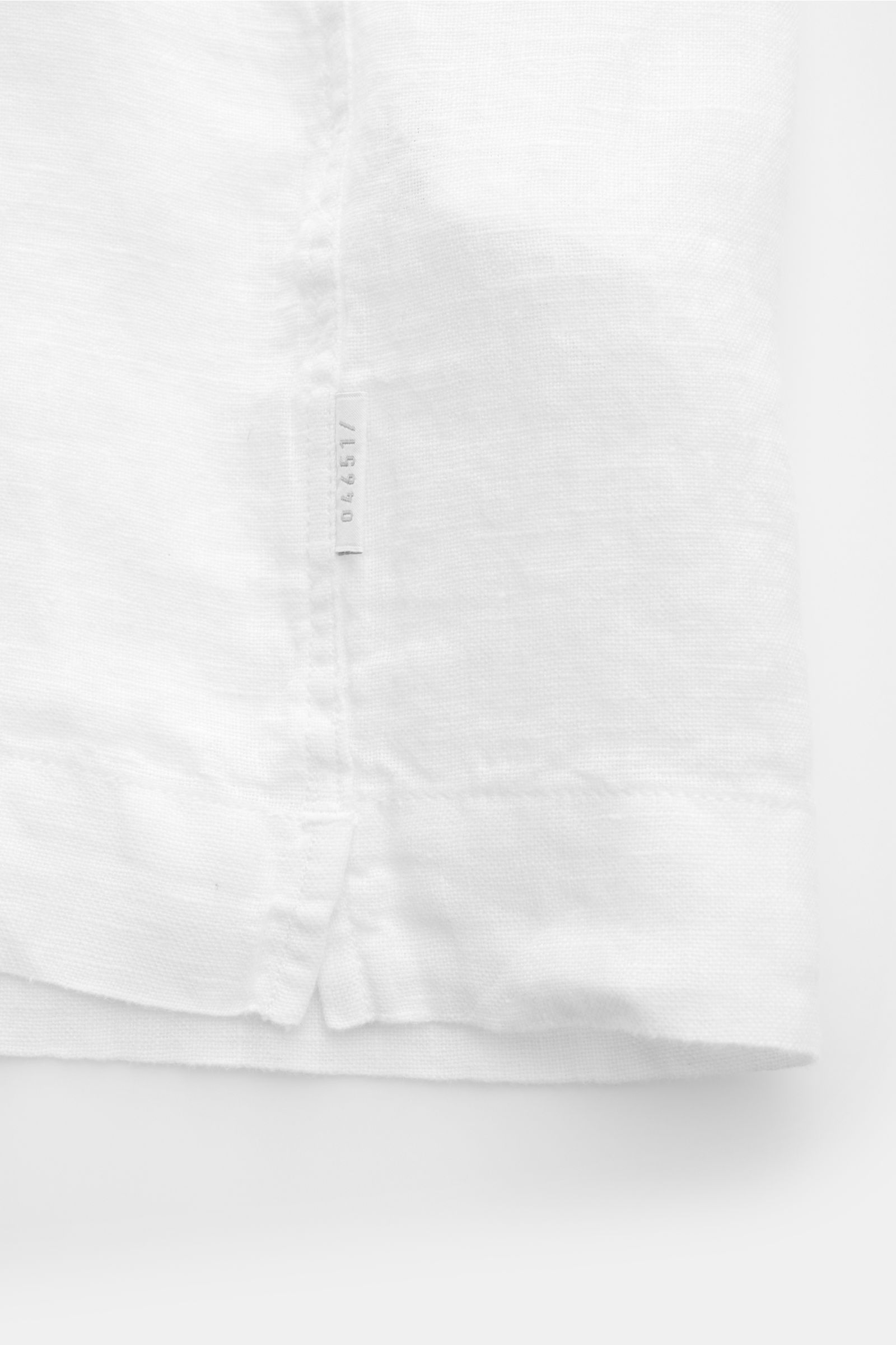 Detailansicht des geraden Saumverlaufs mit kurzen Saumschlitzen und Weblabel vom 04651/ A trip in a bag Leinen-Kurzarmhemd Kubanischer Kragen weiß aus reinem Leinen.