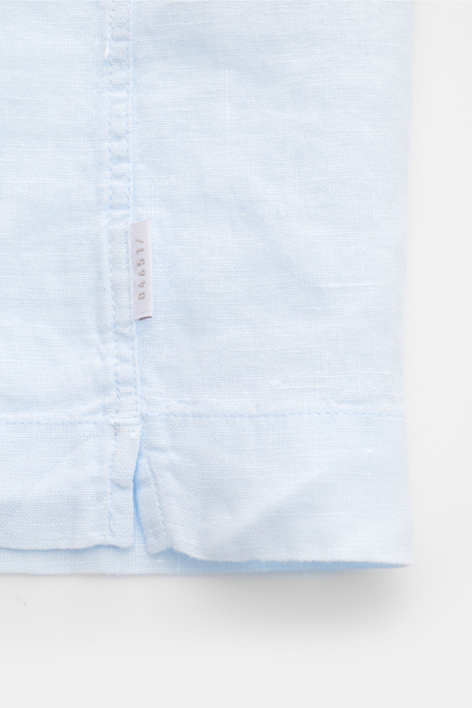 04651/ A trip in a bag Leinen-Kurzarmhemd Kubanischer Kragen pastellblau, Detailansicht Saum mit Weblabel und Saumschlitzen aus reinem Leinen.